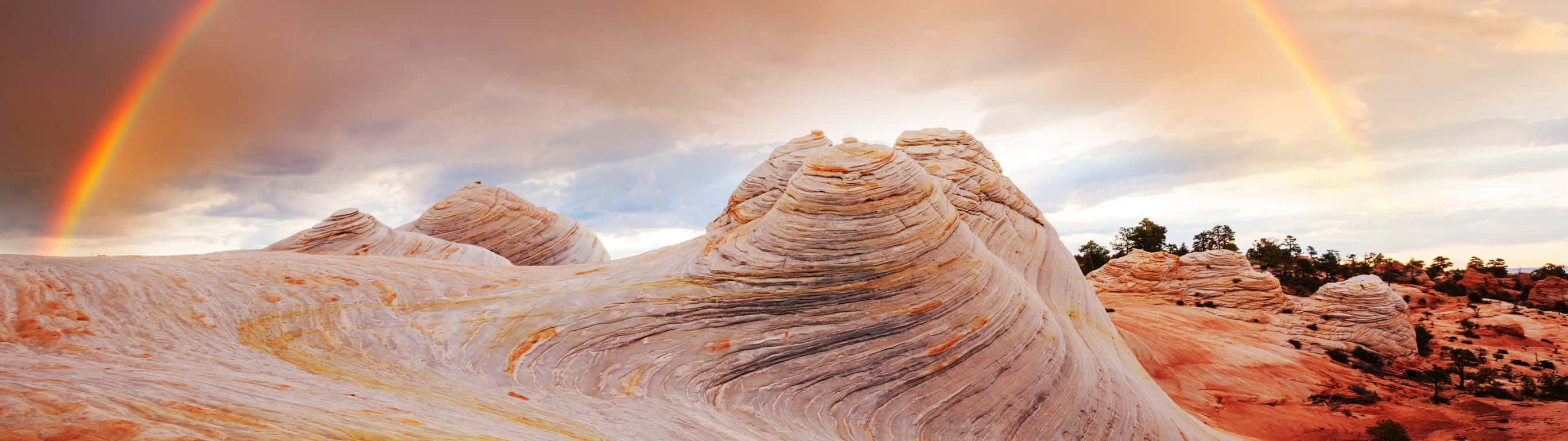 double rainbow, surreal wave-shaped rock formations, dramatic cloudy sky, 2K Desktop Wallpaper
