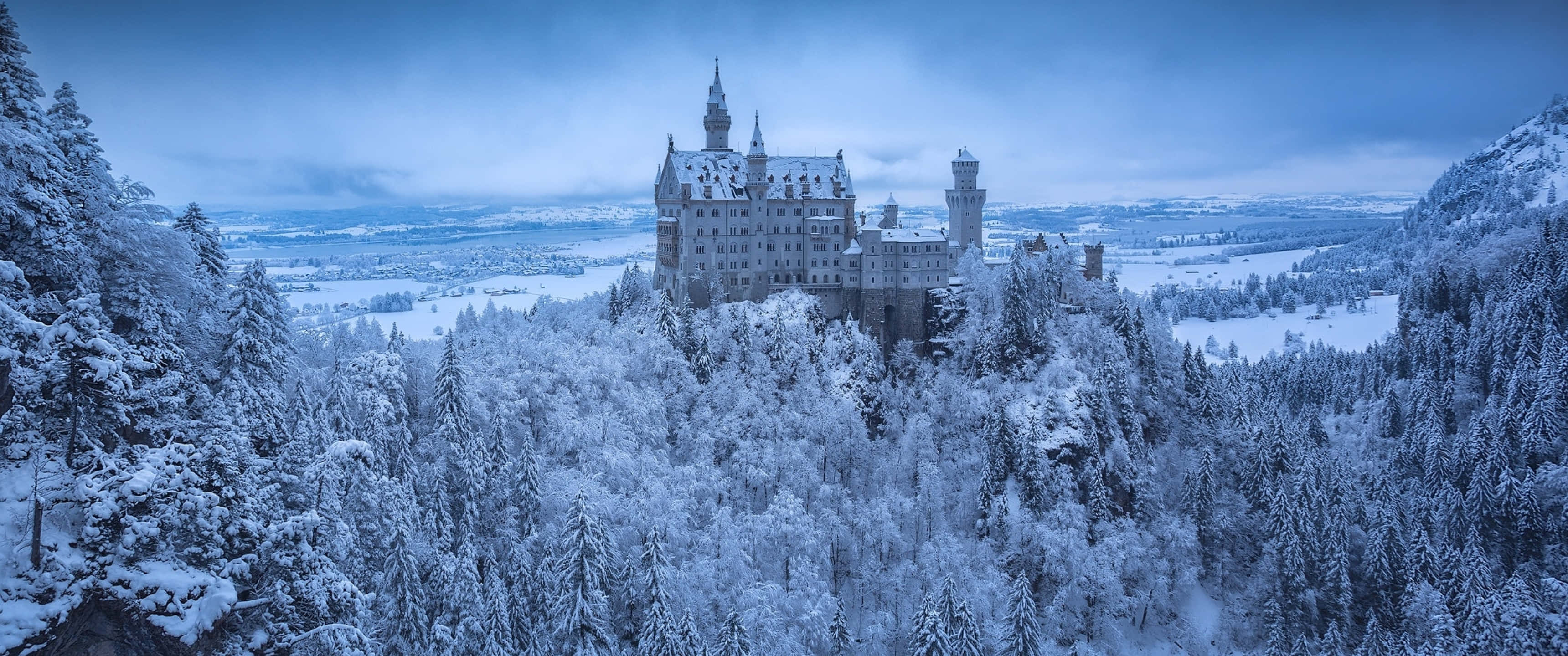 3440x1440 Winter, snow-covered castle, forested hill, 2K Desktop Wallpaper
