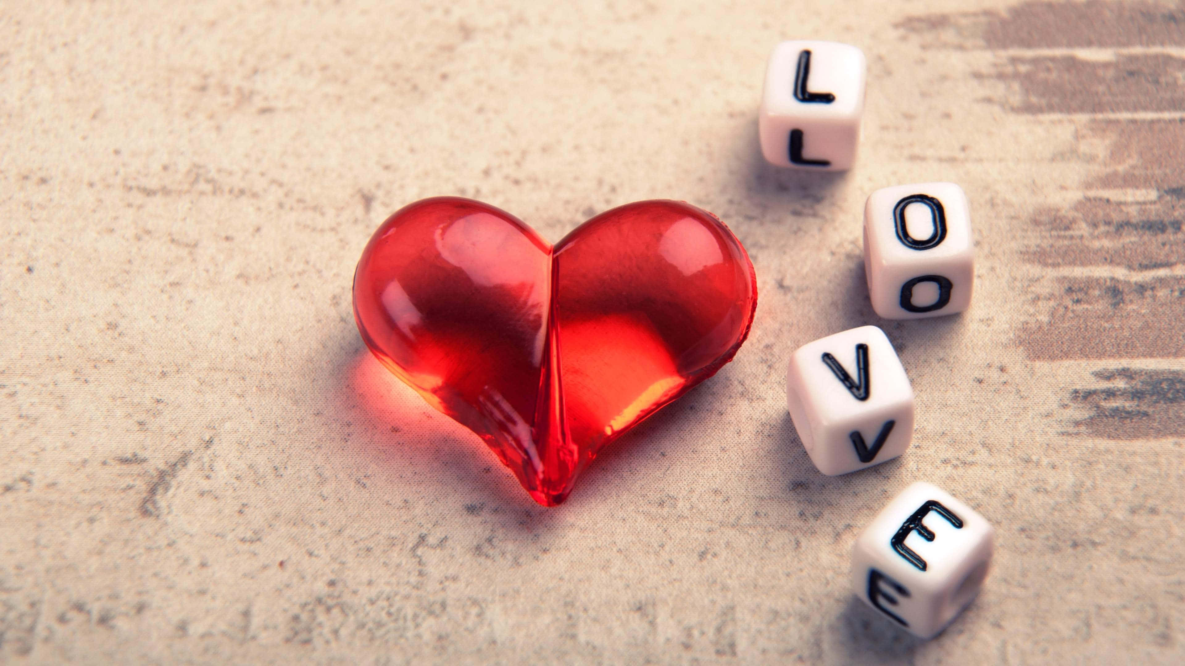glossy red heart-shaped object, white dice spelling love, textured beige surface, 4K Desktop Wallpaper
