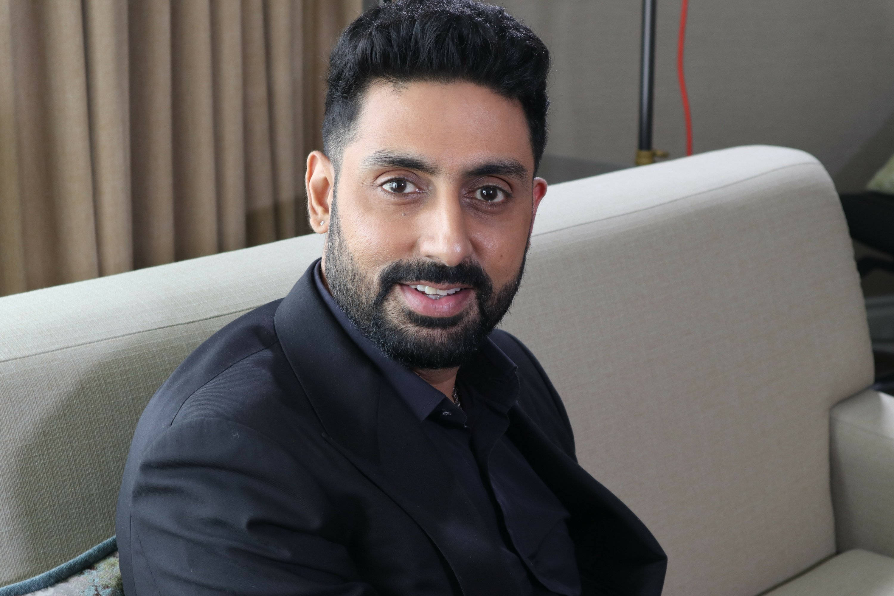 Abhishek Bachchan, beige couch, softly lit indoor setting, 2K Desktop Wallpaper