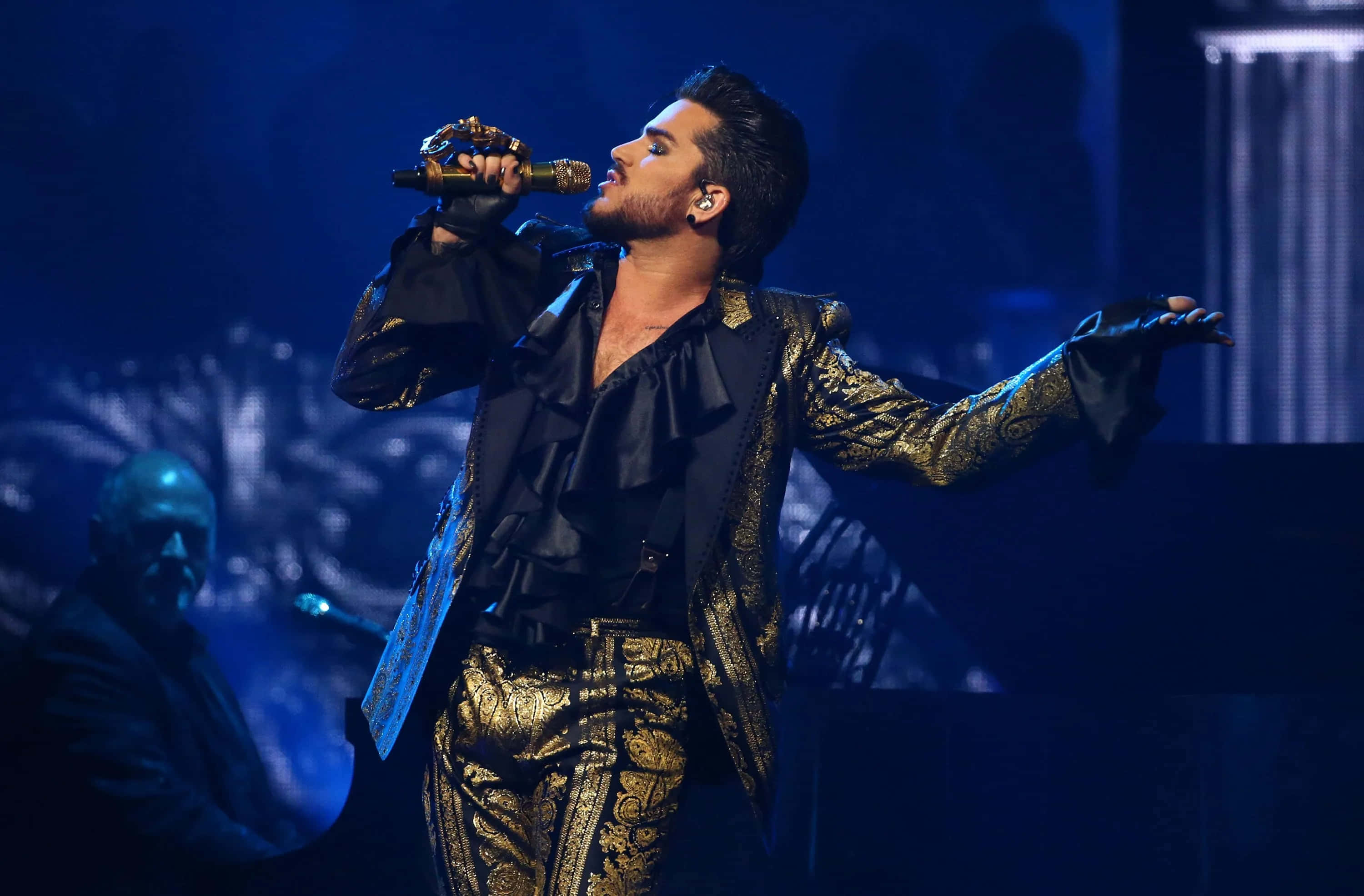 Adam Lambert, gold and black ornate outfit, dimly lit blue stage, 2K Desktop Wallpaper