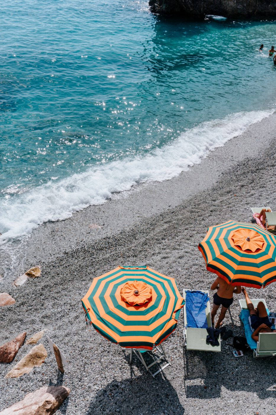 colorful umbrellas, vibrant orange and green striped umbrellas, sunlit black pebble beach, HD Phone Wallpaper