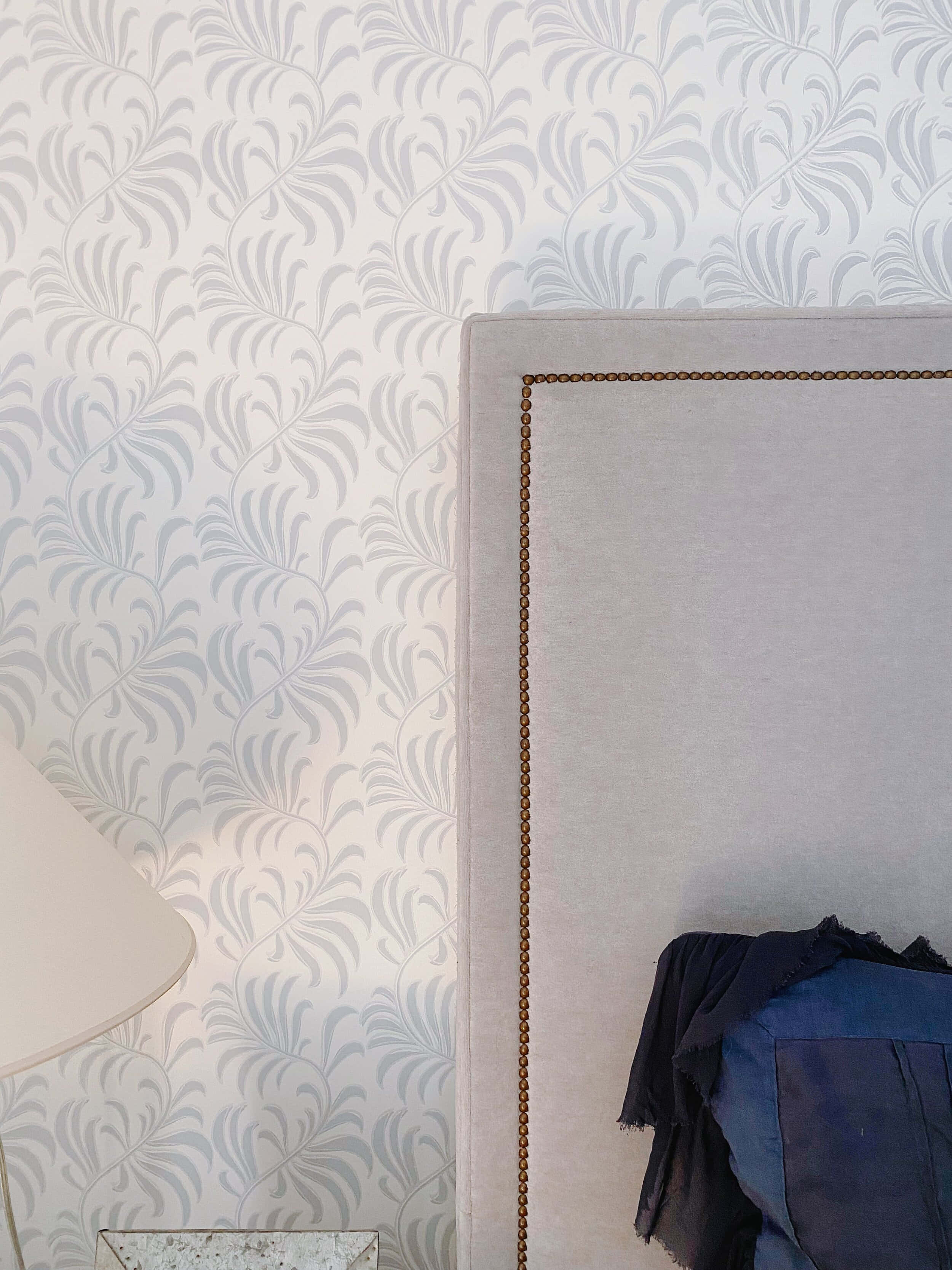 light gray leaf-patterned wallpaper, beige upholstered headboard, brass nailhead trim, 2K Phone Wallpaper