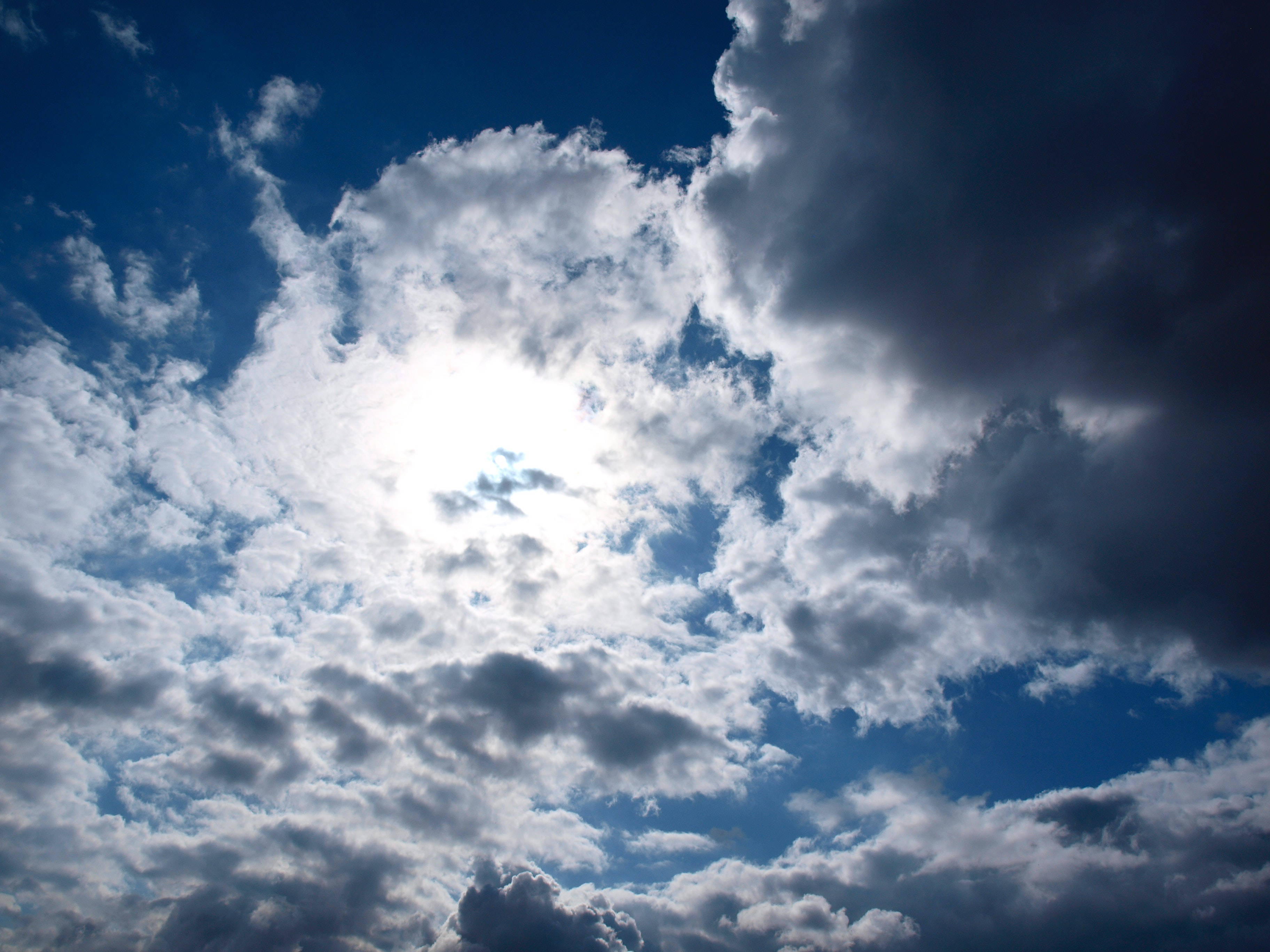 Sunlight, fluffy white and dark gray clouds, deep blue backdrop, 2K Desktop Wallpaper