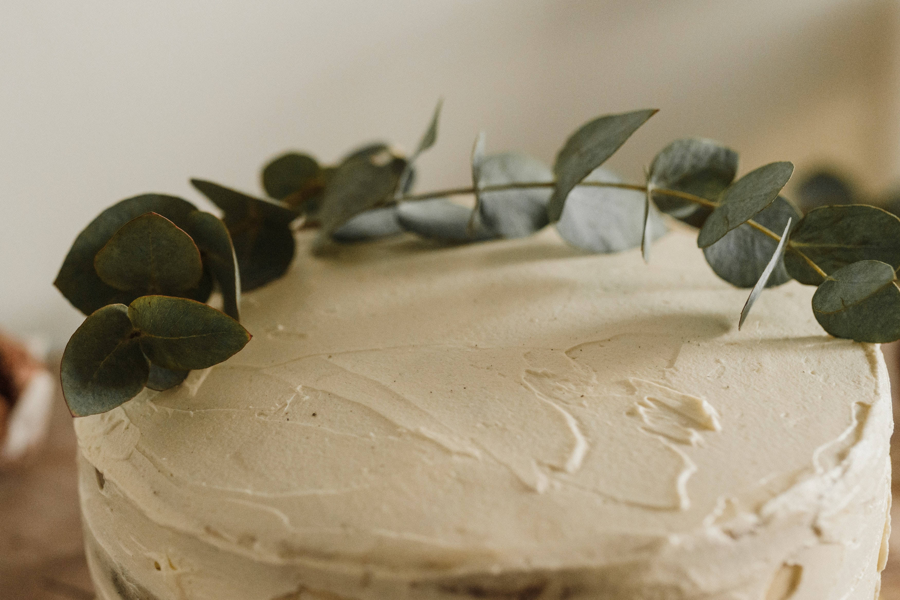 creamy frosted cake, fresh eucalyptus leaf garland, soft blurred background, 2K Desktop Wallpaper