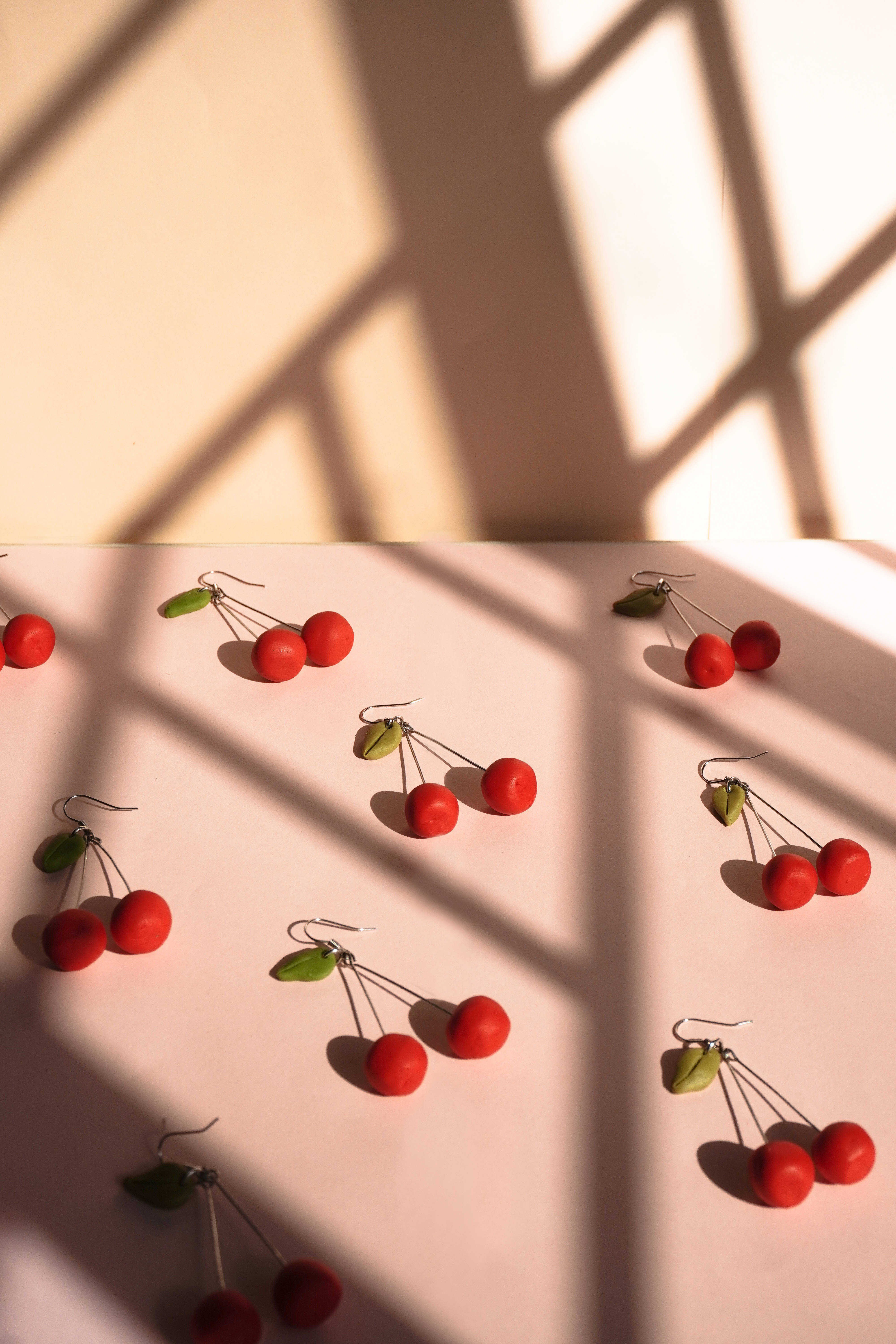 red cherry earrings, pale pink surface, warm window light, 5K Phone Wallpaper