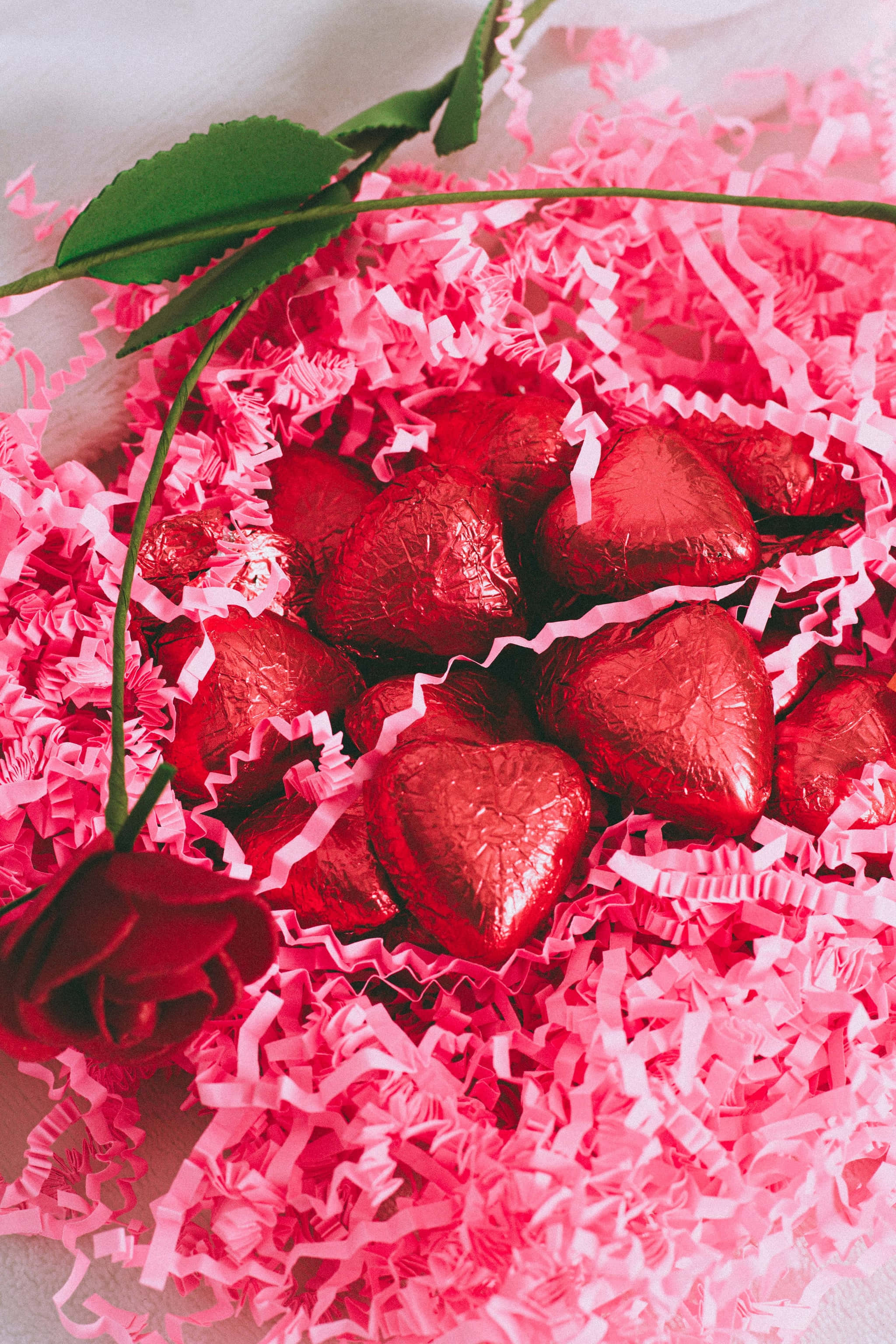 Heart-shaped chocolates, shiny red foil, pink shredded paper, 2K Phone Wallpaper