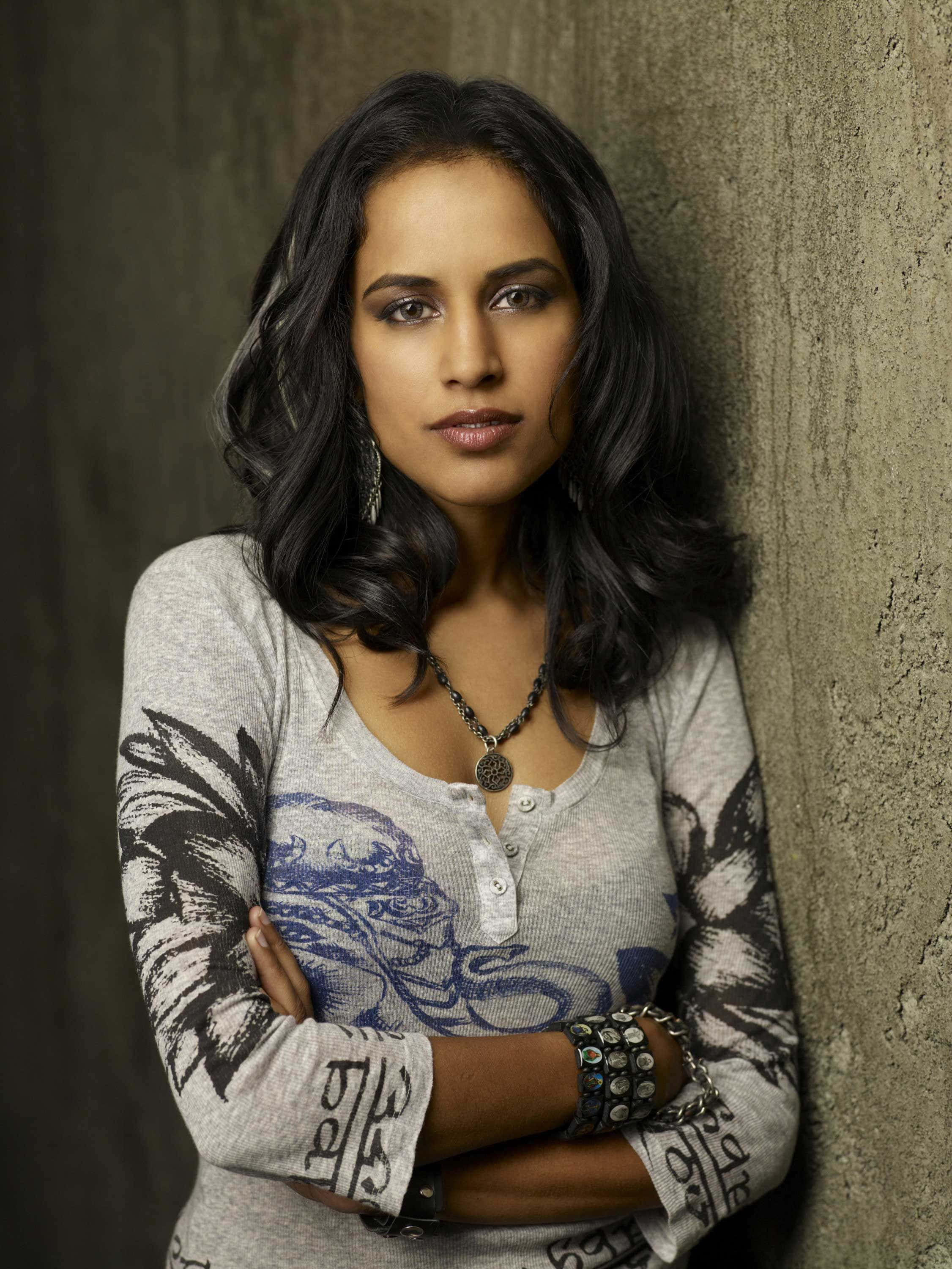 Agam Darshi, dark wavy hair, textured concrete wall, 2K Phone Wallpaper