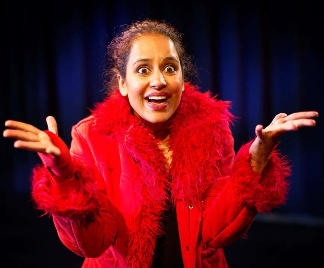 Agam Darshi, vibrant red feathered coat, dark blue curtain backdrop, SD Desktop Wallpaper