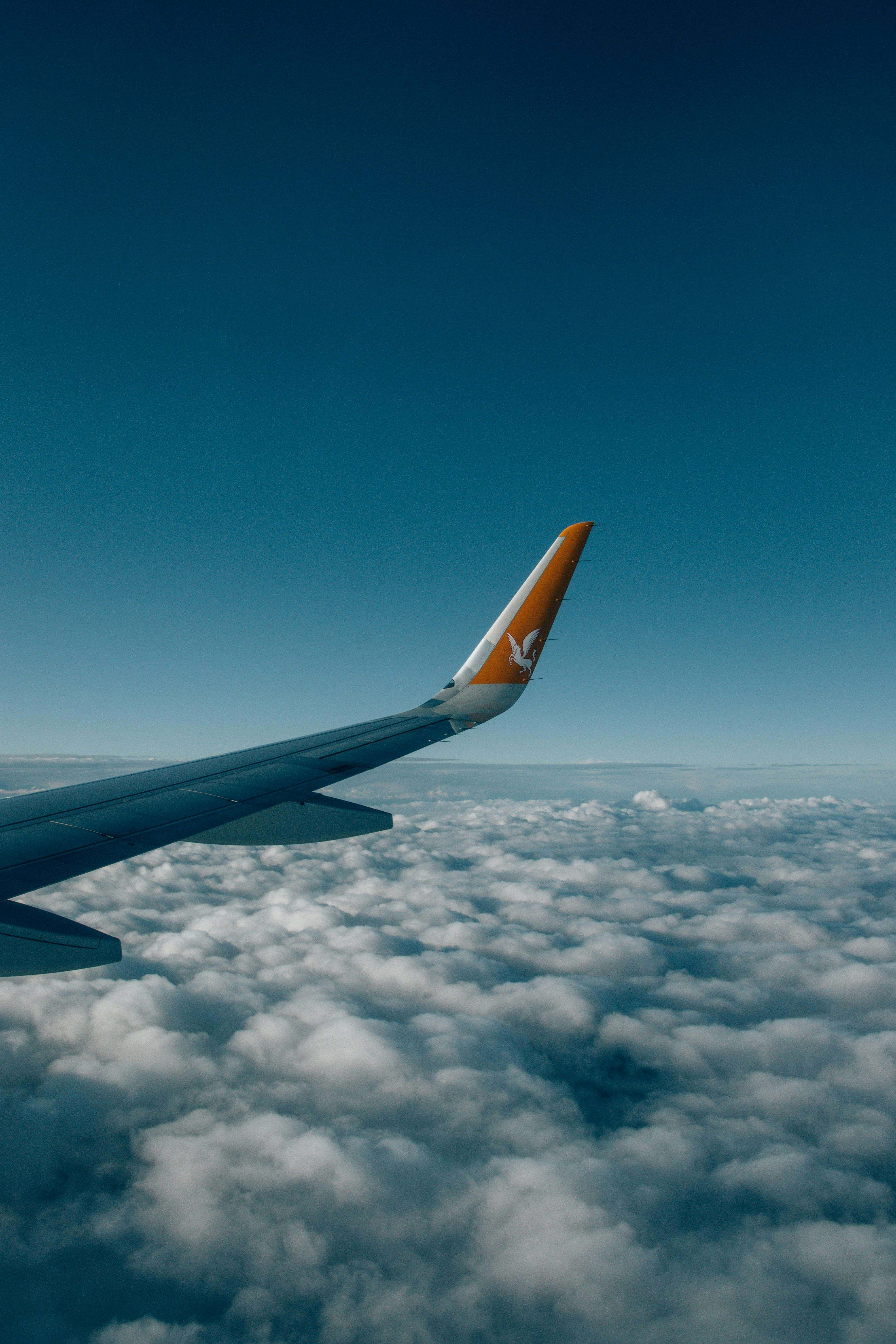 airplane wing, orange tail logo, fluffy white clouds, 5K Phone Wallpaper
