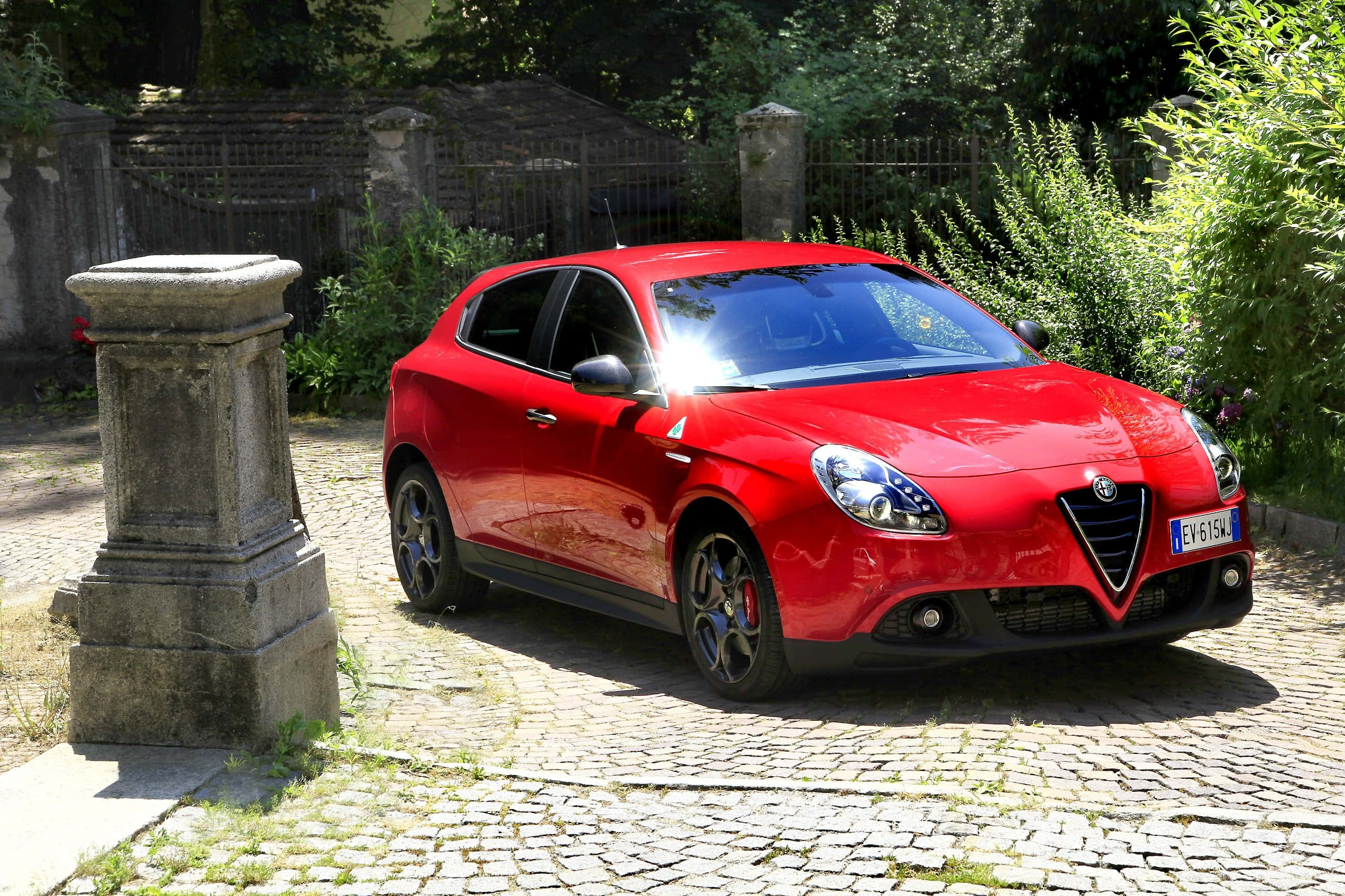 Alfa Romeo Giulietta, vibrant red, sunlit cobblestone driveway, 2K Desktop Wallpaper