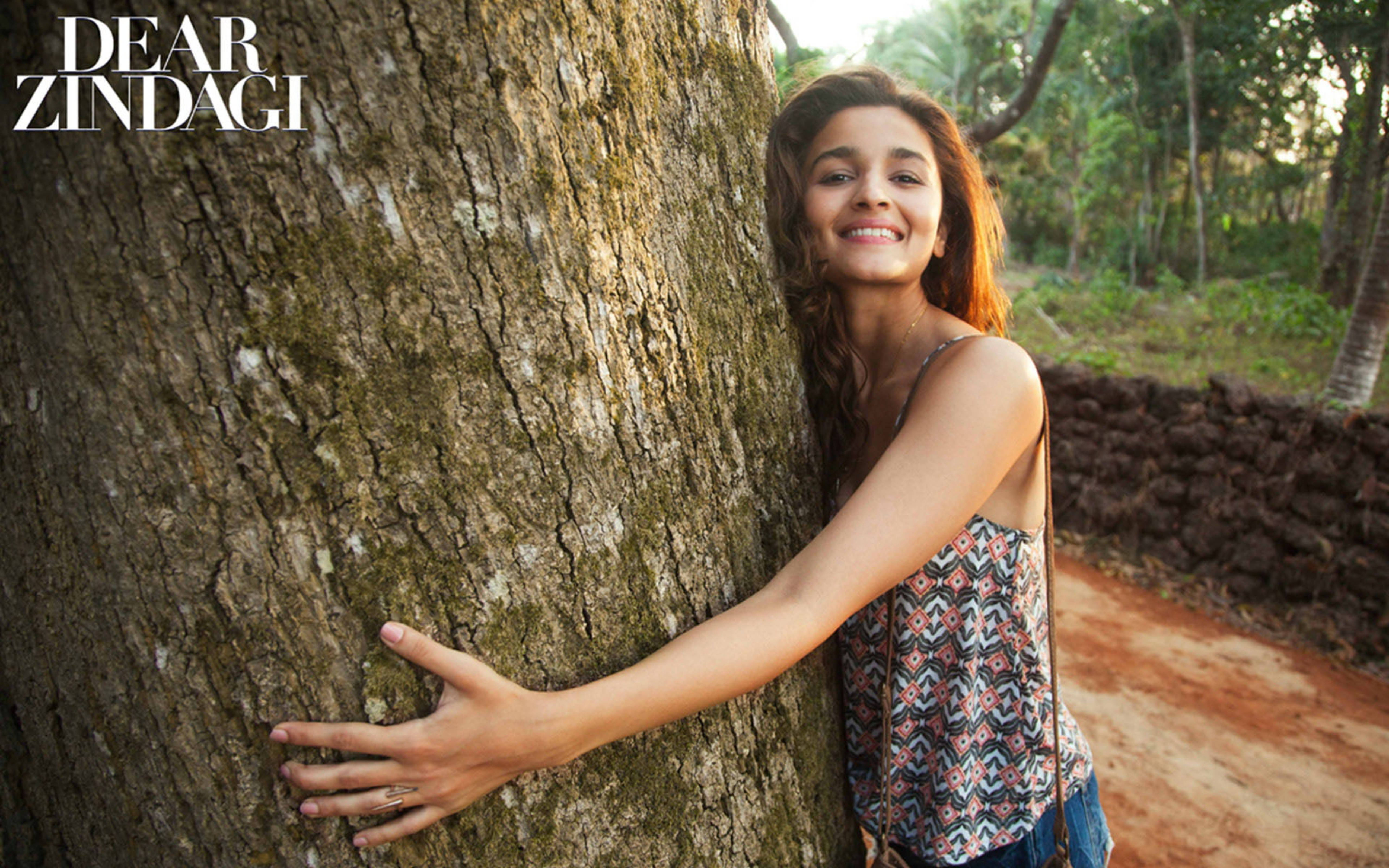 Alia Bhatt, sunlit forest clearing, massive textured tree trunk, 5K Desktop Wallpaper