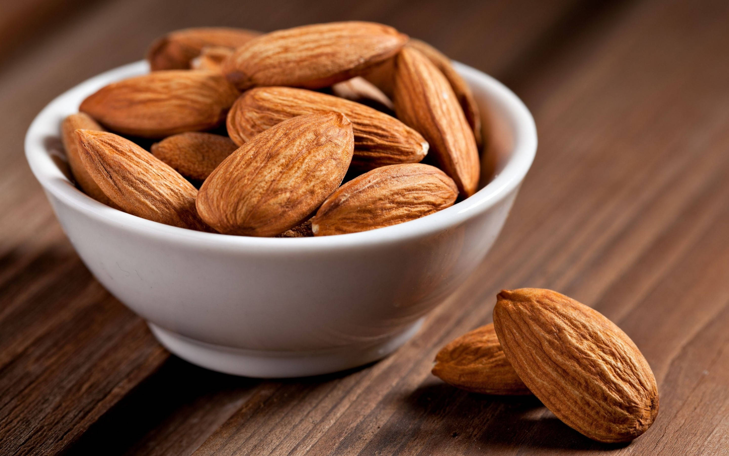 white ceramic bowl, textured brown almonds, dark wooden surface, 2K Desktop Wallpaper