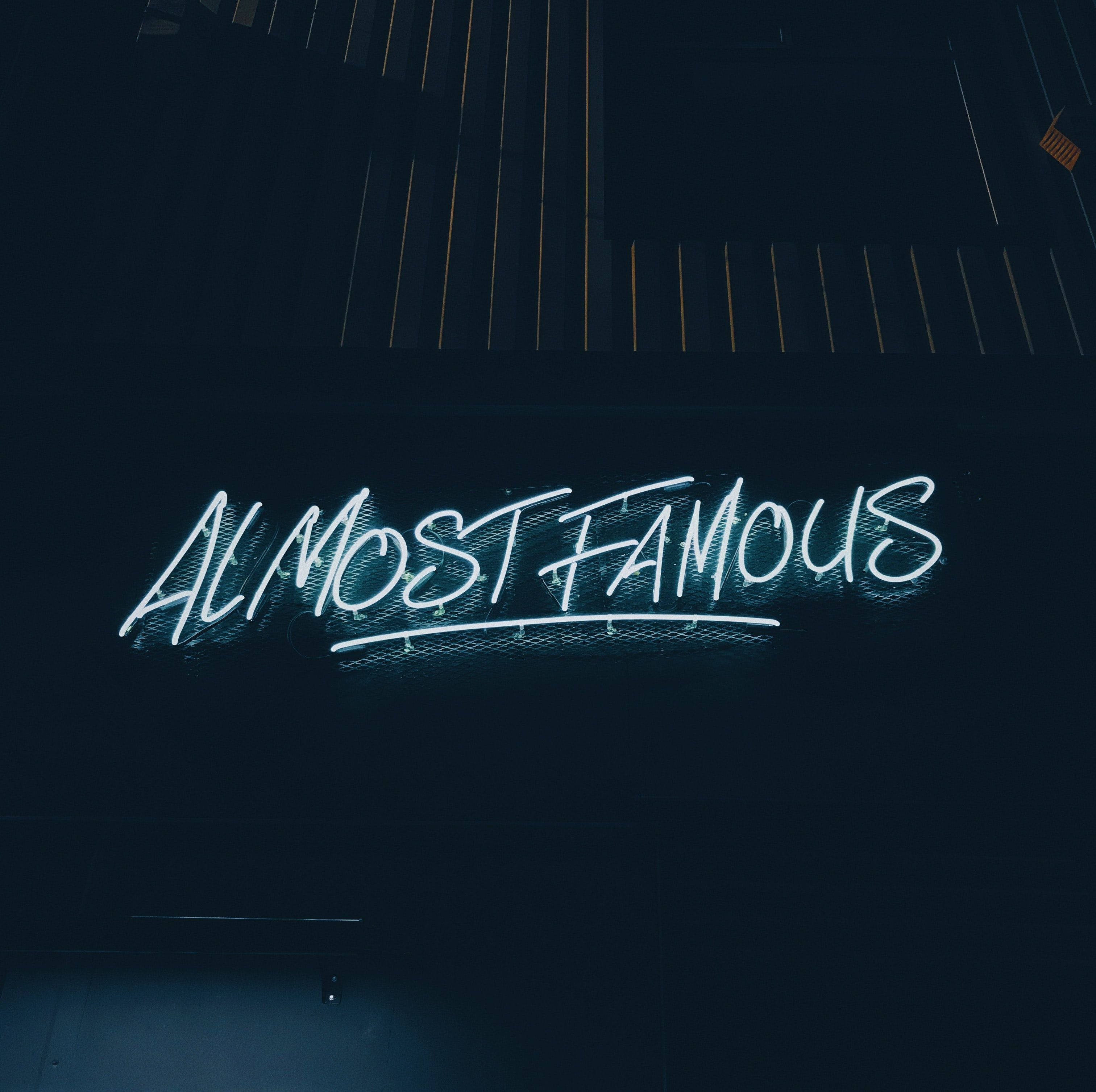 ALMOST FAMOUS, glowing blue neon sign, dark urban wall, 2K Desktop Wallpaper