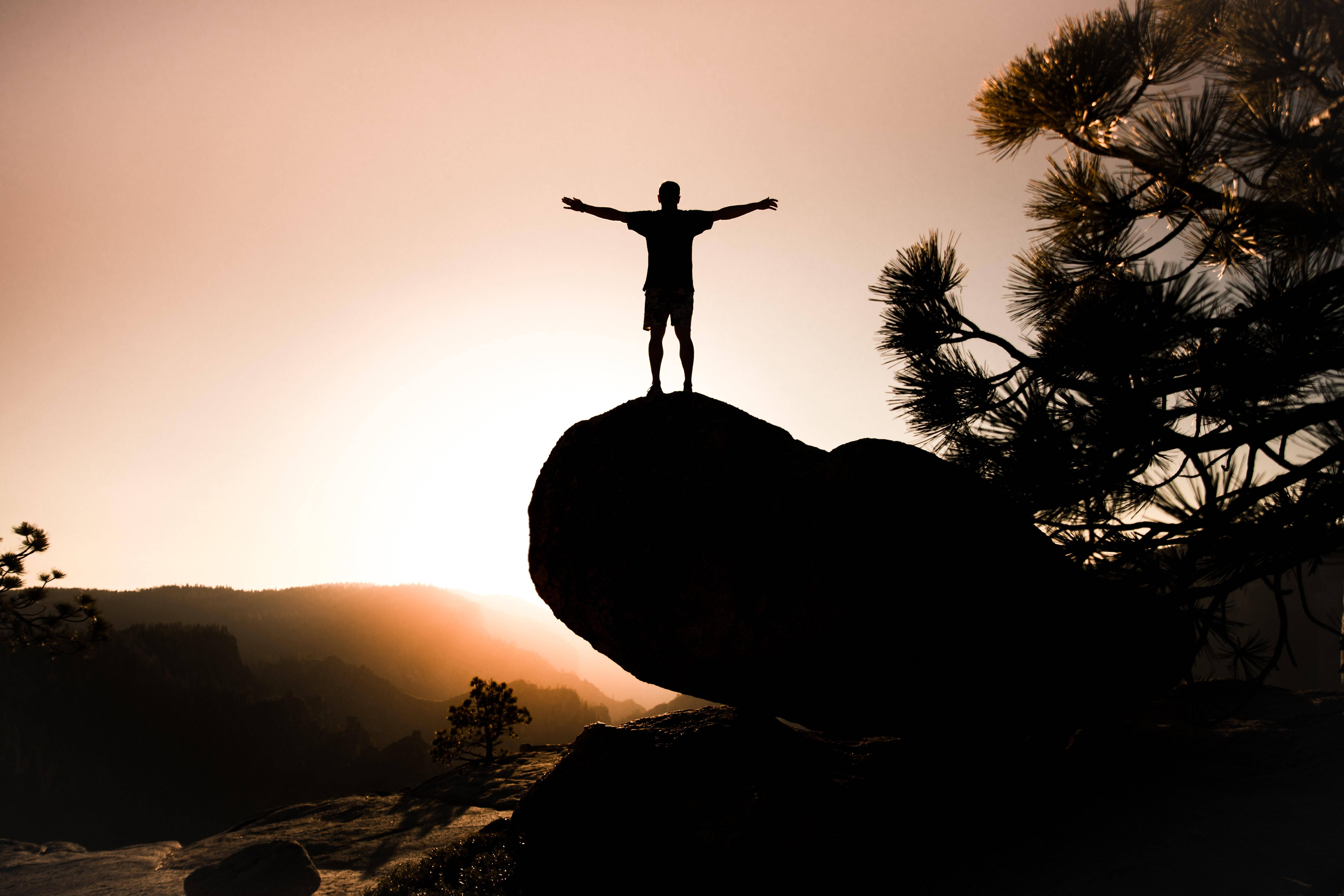 Man With Open Arms Alone Phone, rocky outcrop, glowing sunset sky, 5K Desktop Wallpaper