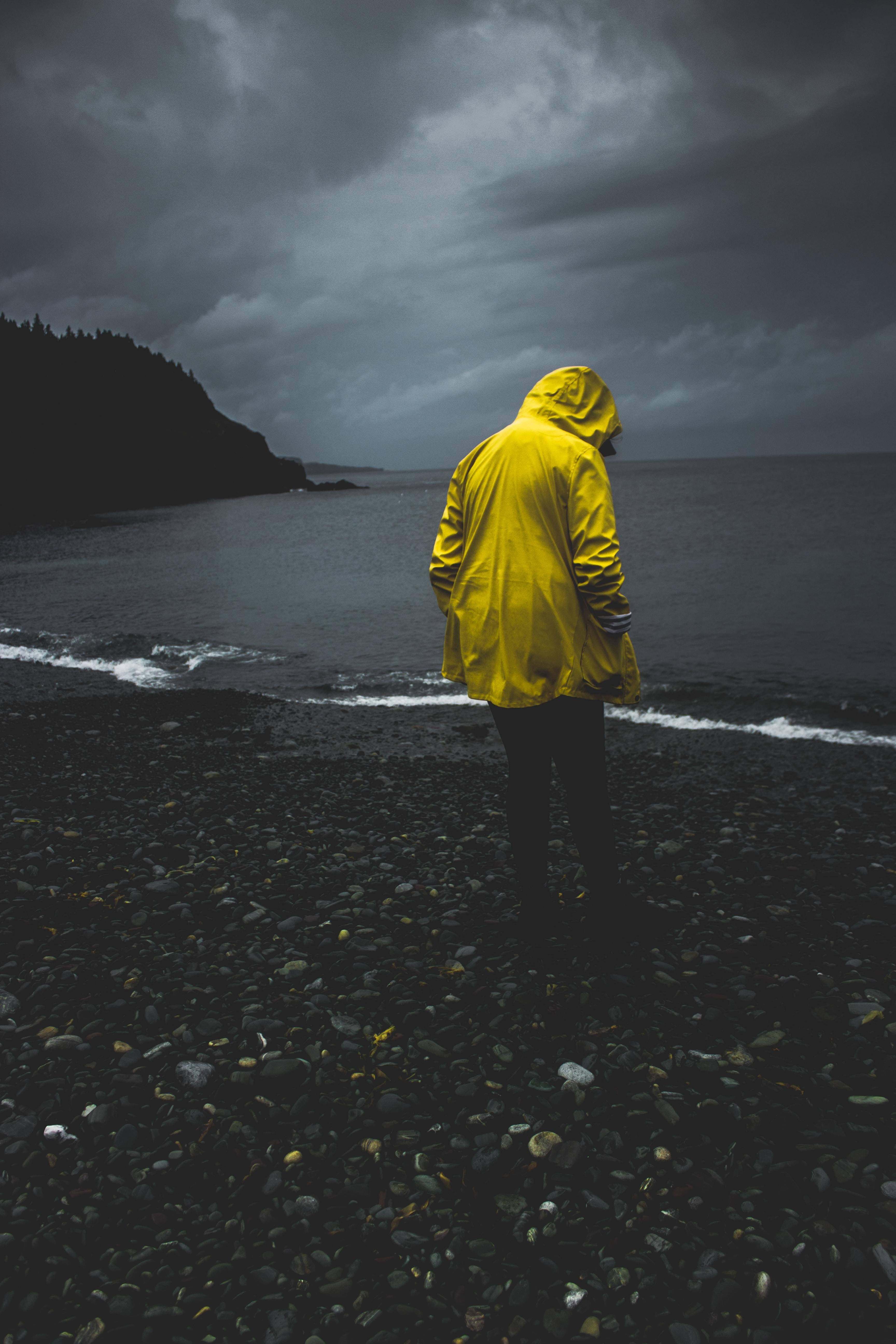 man, rocky seashore, bright yellow raincoat, 5K Phone Wallpaper
