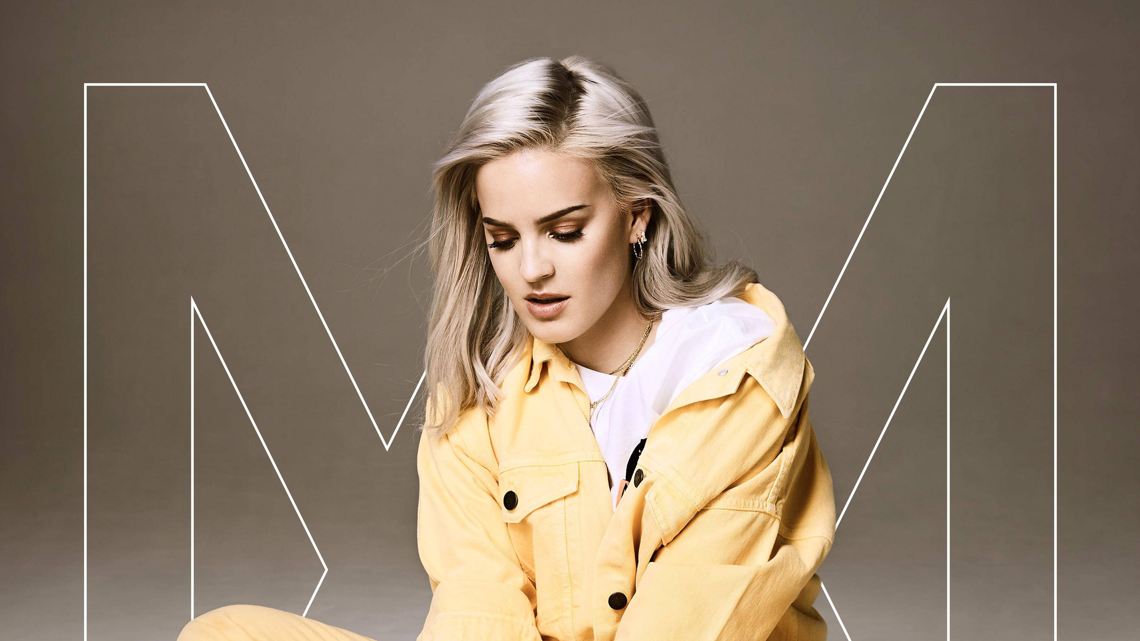 Anne Marie, yellow jacket, large white outlined letter M, 4K Desktop Wallpaper