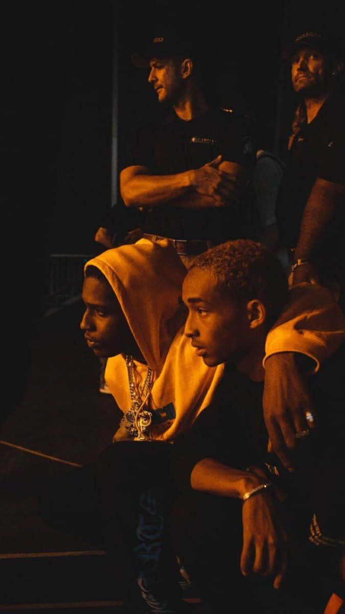 Asap Rocky Testing, dim orange-lit setting, serious expressions, SD Phone Wallpaper