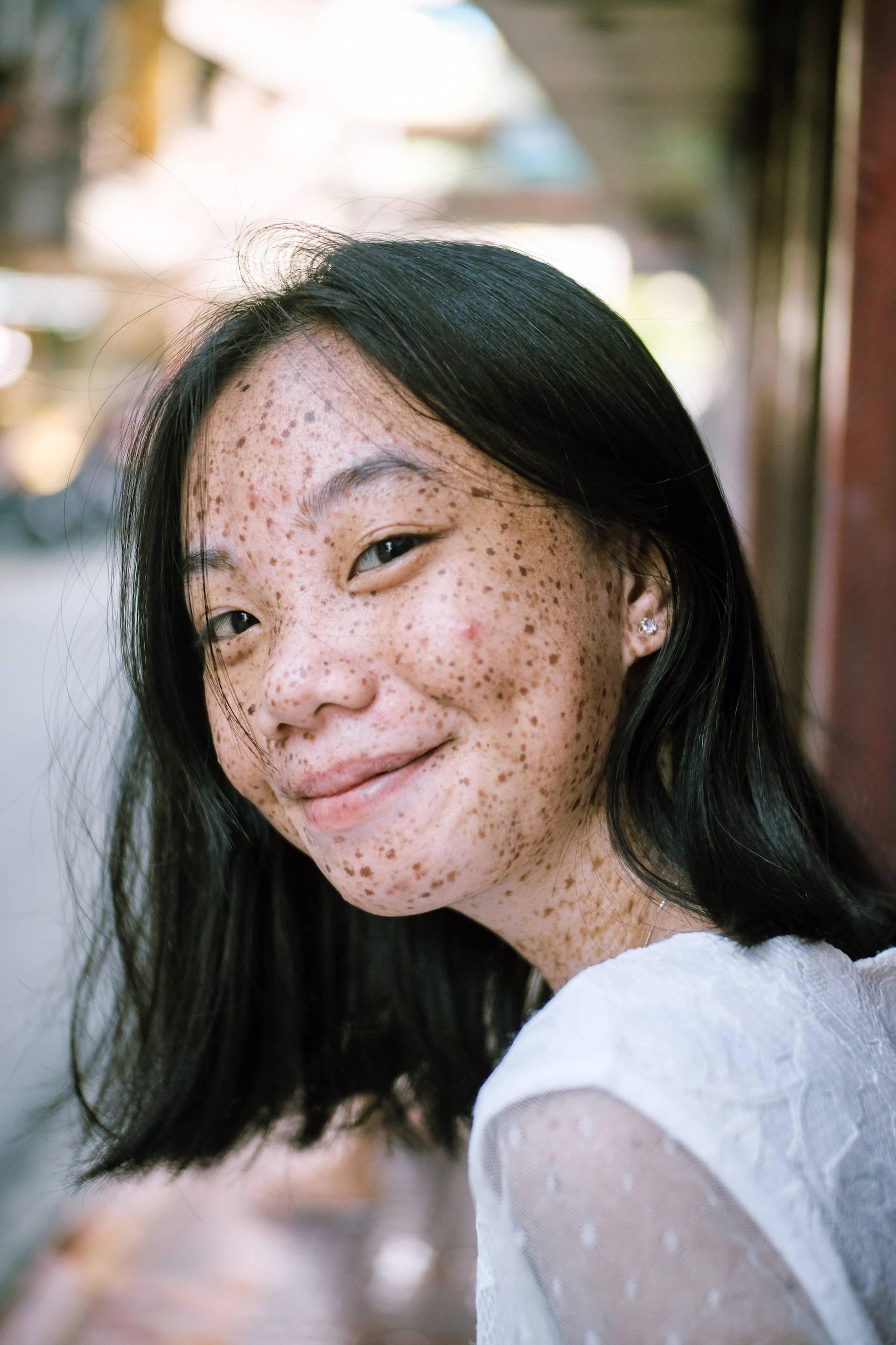 Asian woman, freckles, sunlit urban alleyway, 2K Phone Wallpaper