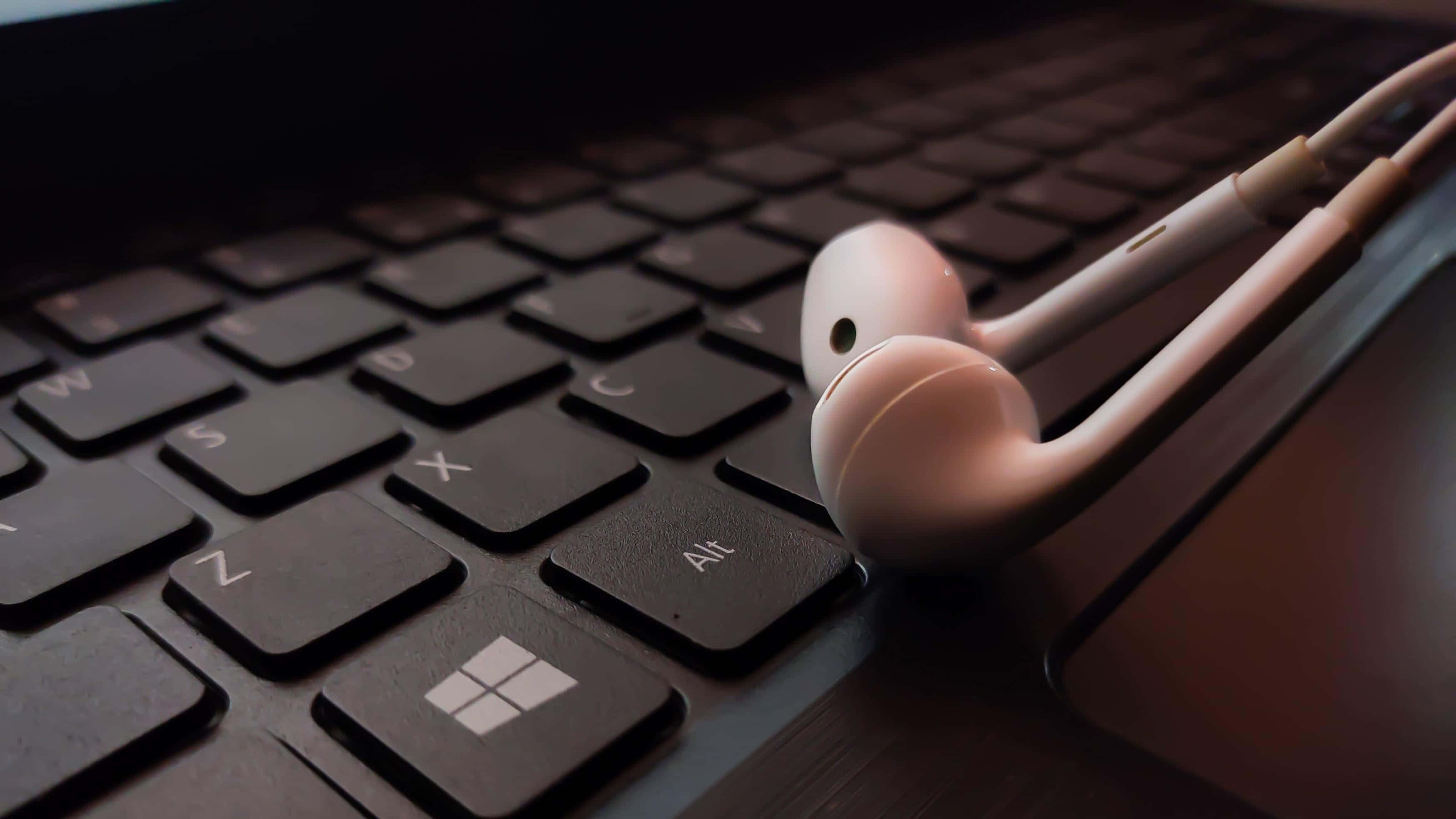 Windows logo key, dark laptop keyboard, white earbuds, 2K Desktop Wallpaper