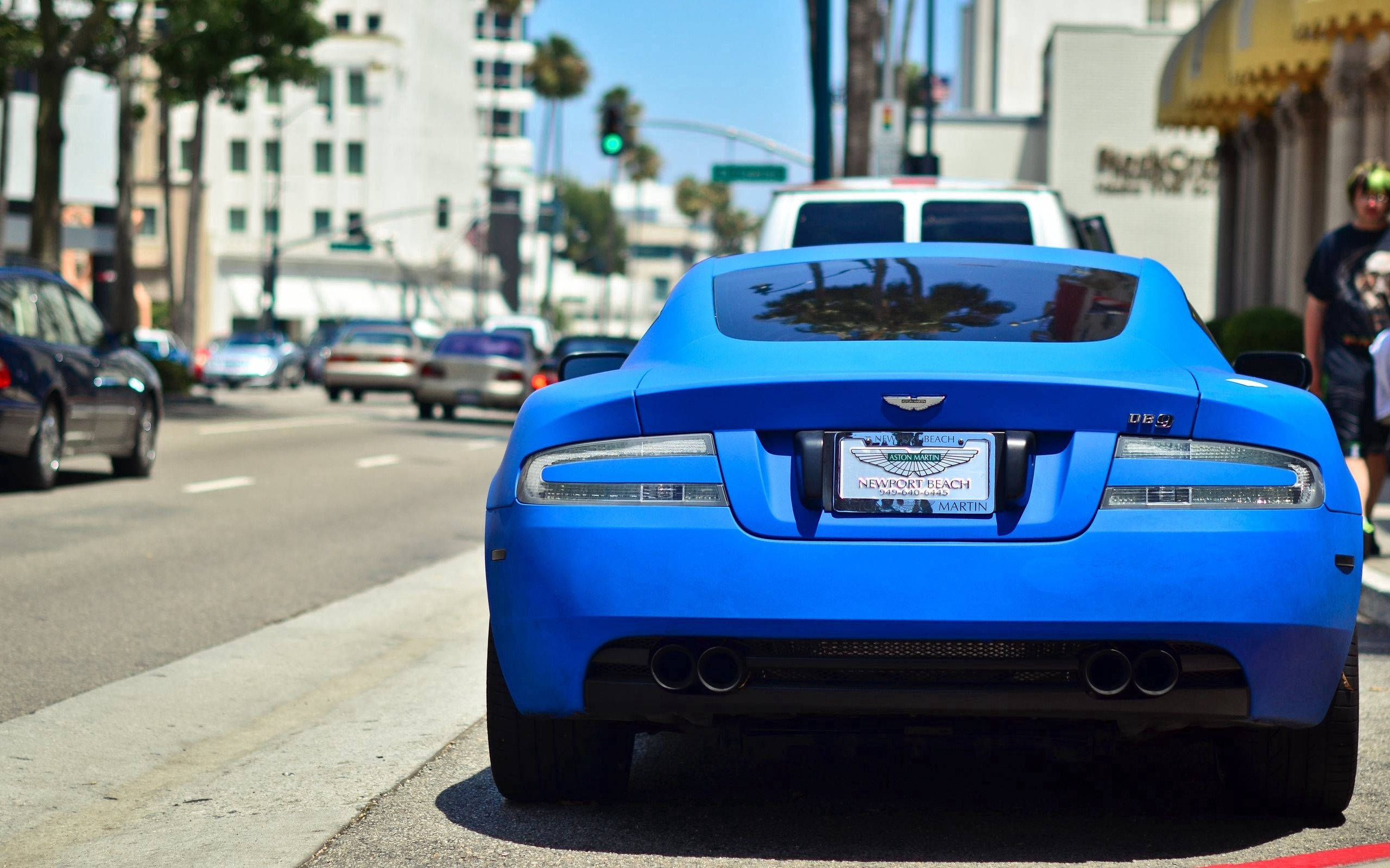 Aston Martin DB9, vibrant blue, sunny city street, 2K Desktop Wallpaper