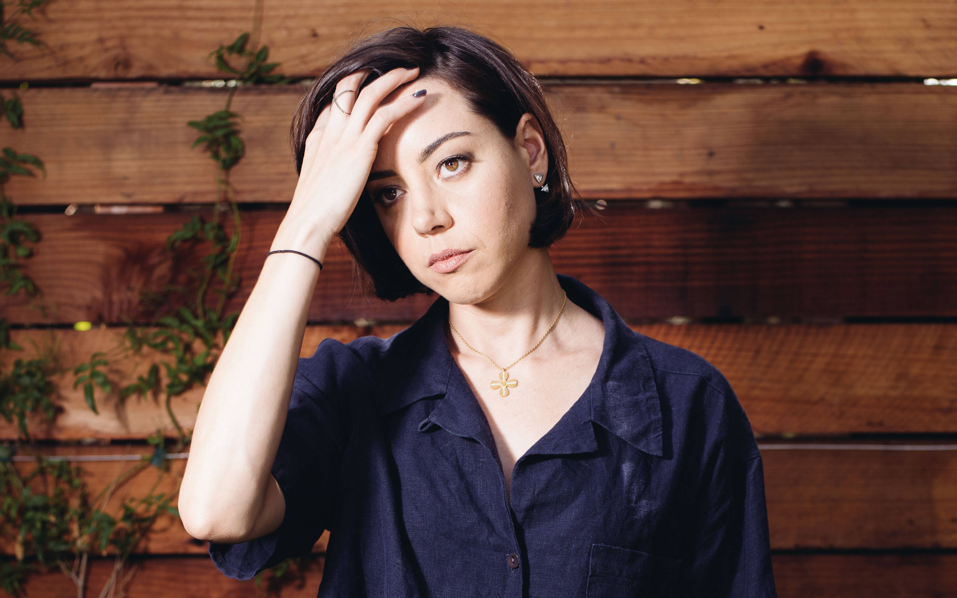 Aubrey Plaza, short dark hair, rustic wooden wall, 2K Desktop Wallpaper