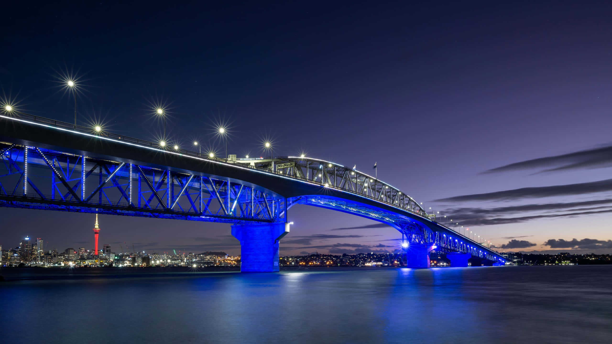 Auckland Harbour Bridge, vibrant blue lights, calm water, 2K Desktop Wallpaper