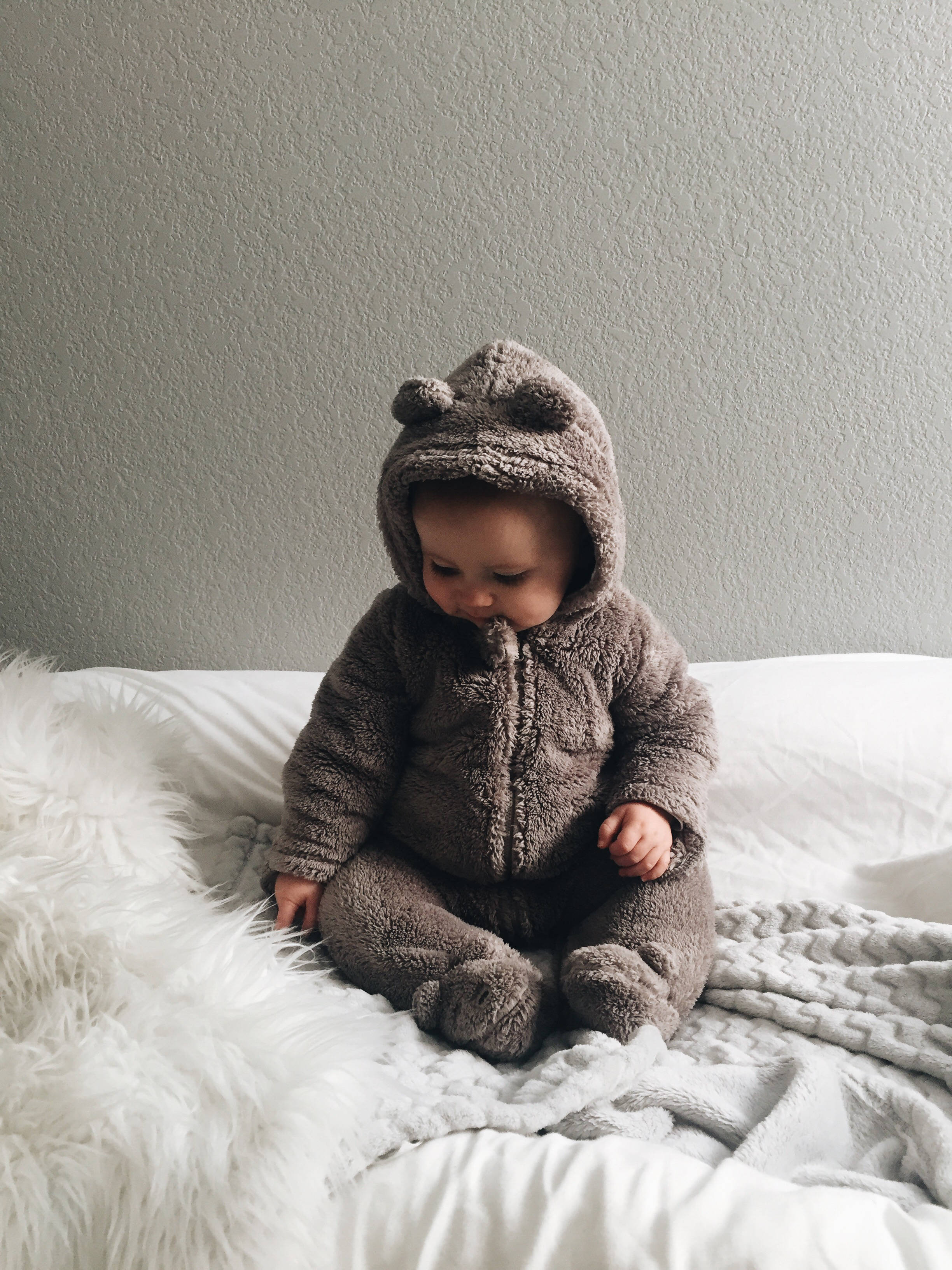 fluffy brown bear onesie, soft white bedspread, plain gray wall, 2K Phone Wallpaper