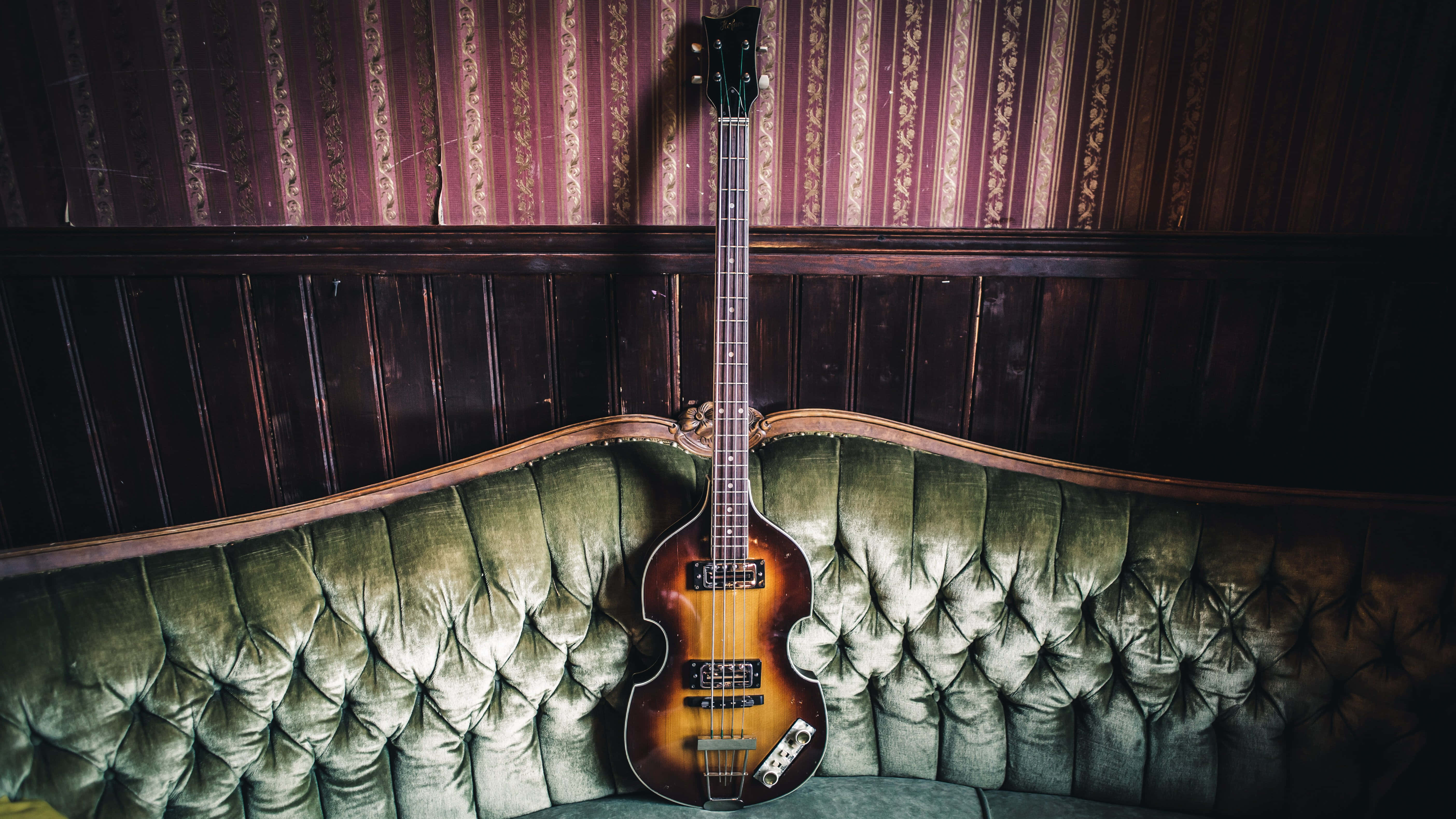 vintage sunburst bass guitar, tufted green velvet sofa, richly patterned burgundy wallpaper, 5K Desktop Wallpaper