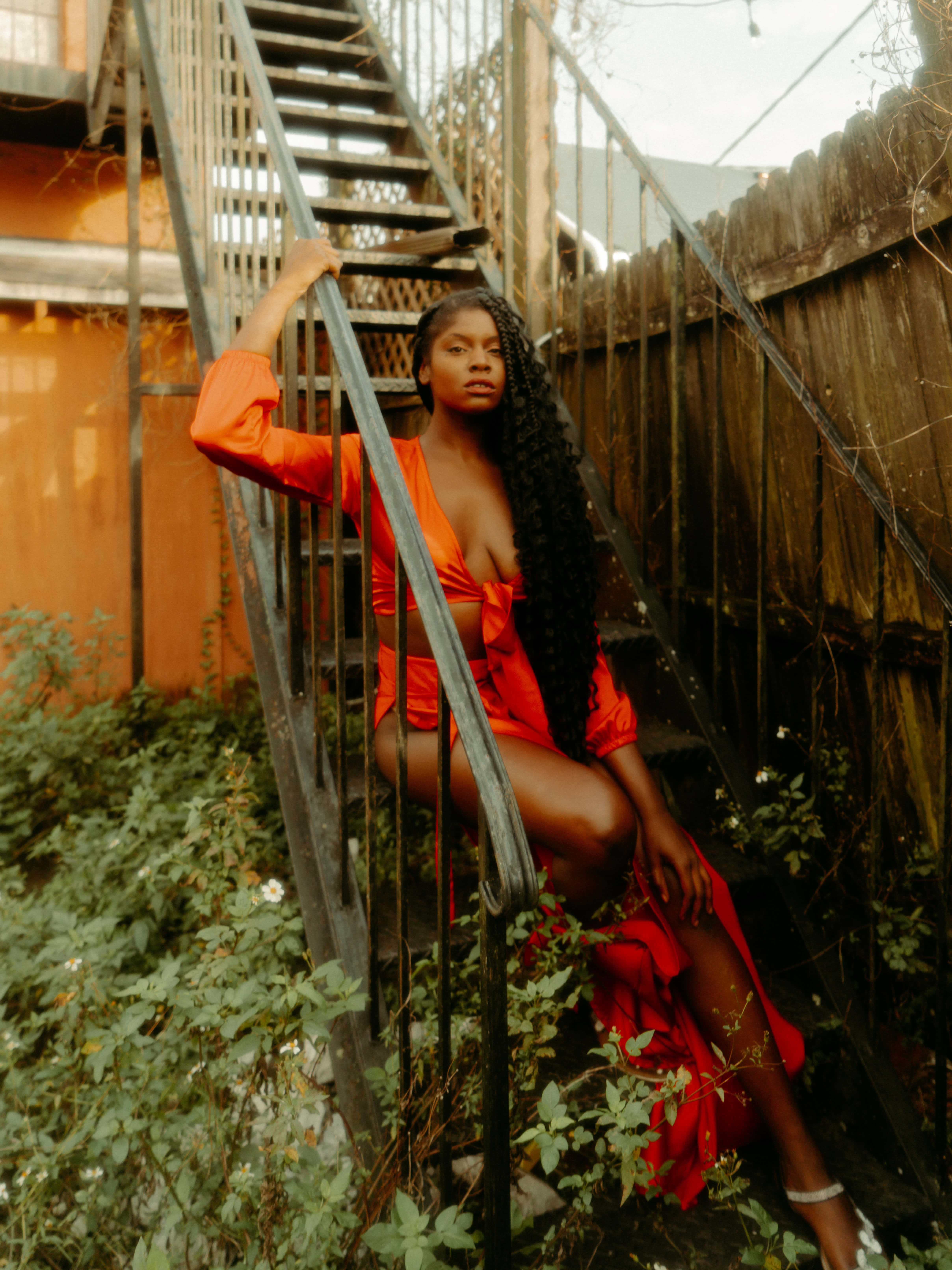 vibrant orange dress, weathered metal staircase, lush greenery, 5K Phone Wallpaper