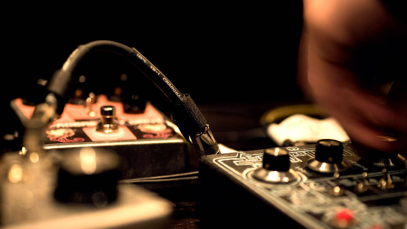black guitar effects pedal, glowing red indicator, warm dim lighting, HD Desktop Wallpaper
