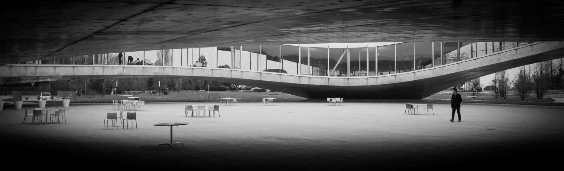 vast curved concrete structure, scattered chairs and tables, stark black and white urban plaza, Full HD Desktop Wallpaper
