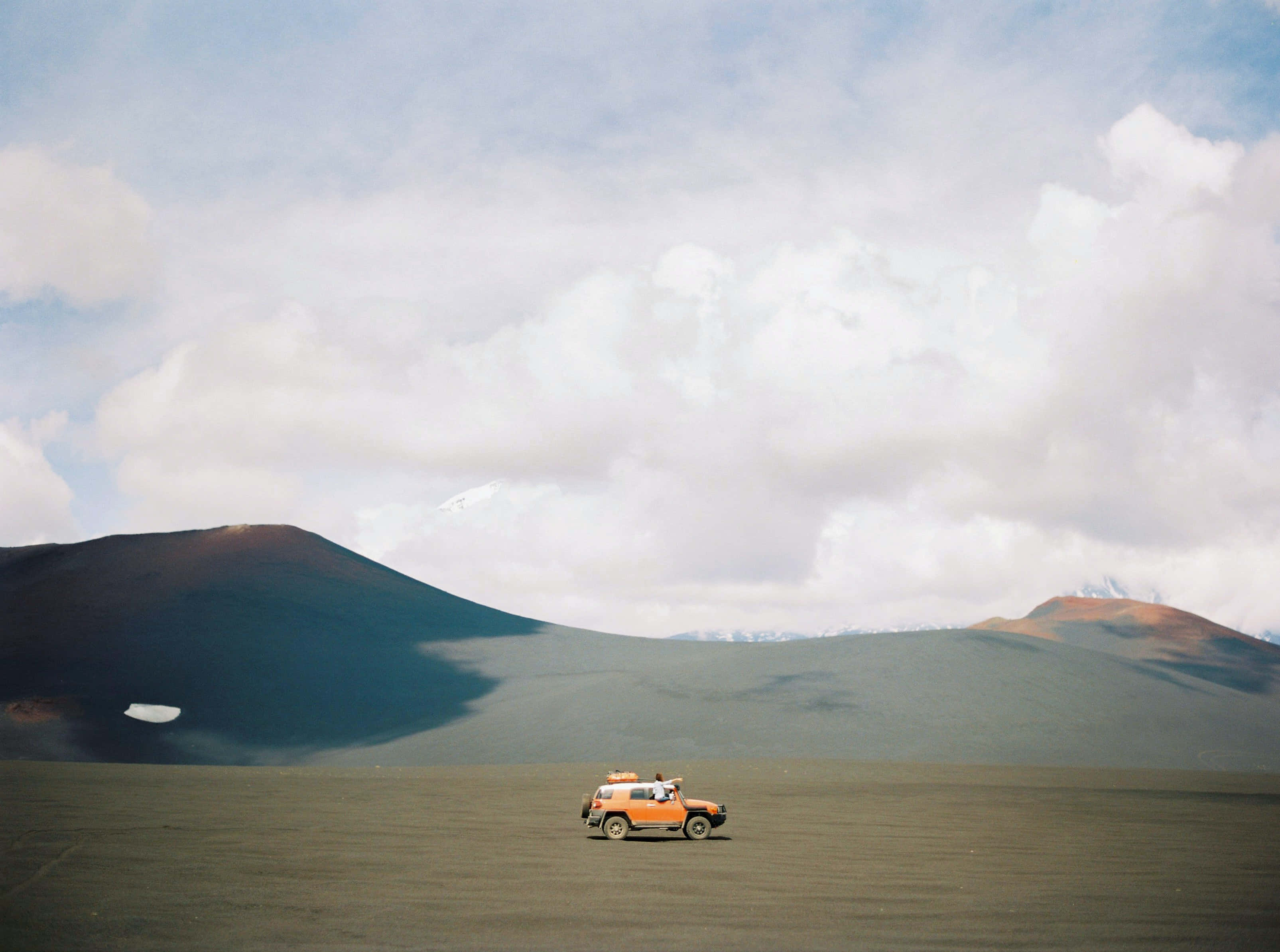 orange off-road vehicle, vast volcanic plain, cloudy sky, 2K Desktop Wallpaper