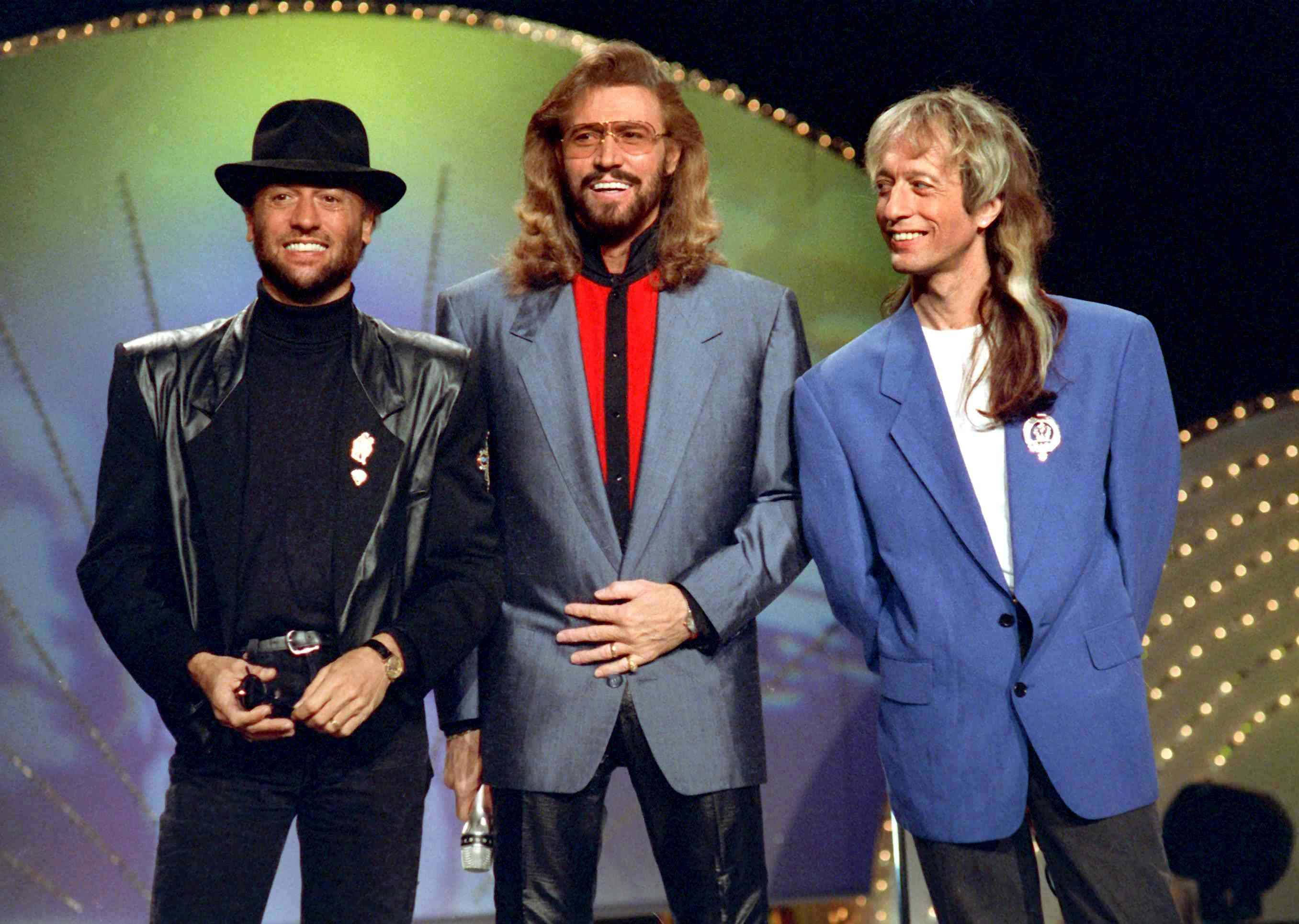 Bee Gees, 1980s glam rock attire, lit stage, 2K Desktop Wallpaper
