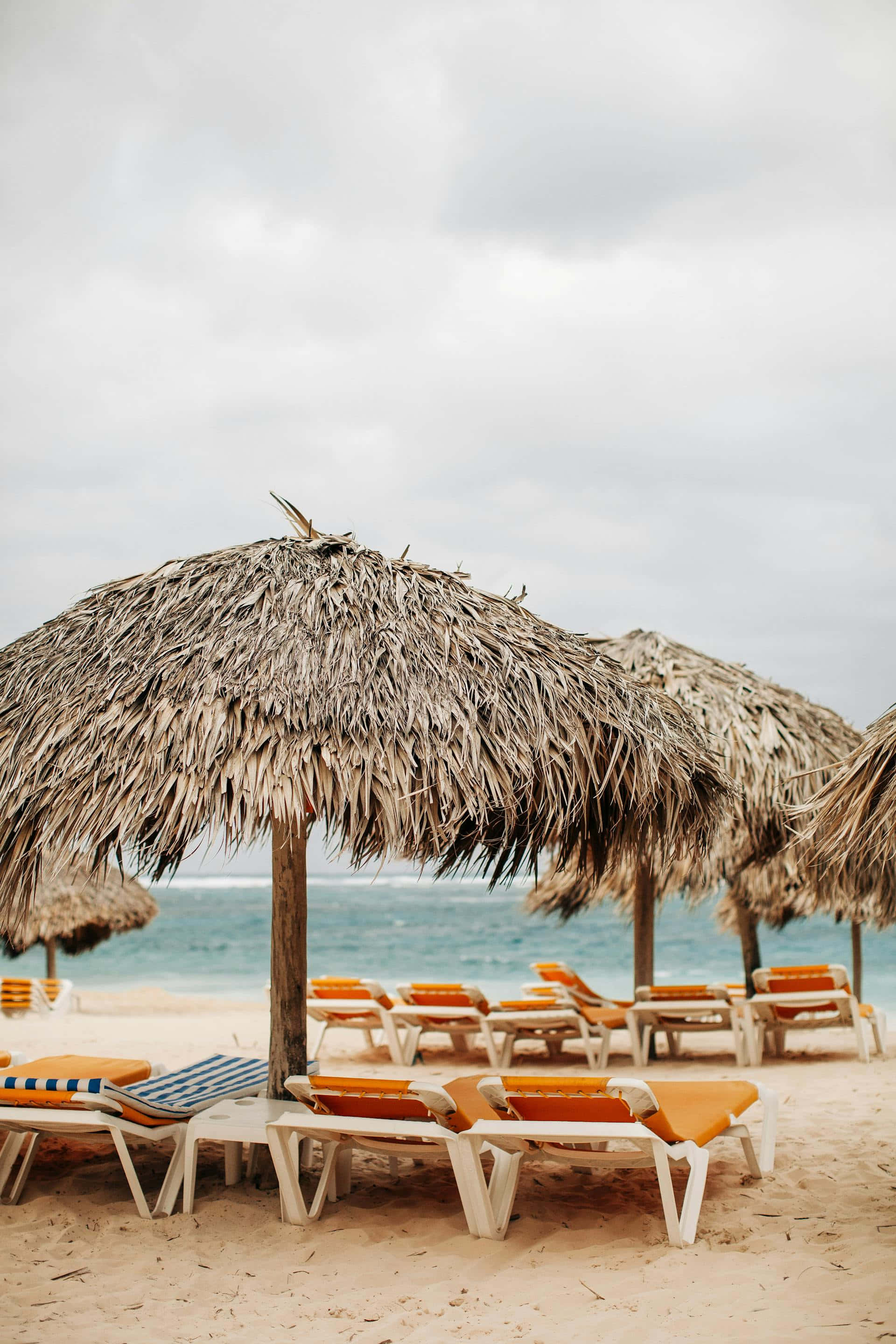beige beach umbrellasand loungers, orange lounge chairs, thatched umbrellas, 2K Phone Wallpaper