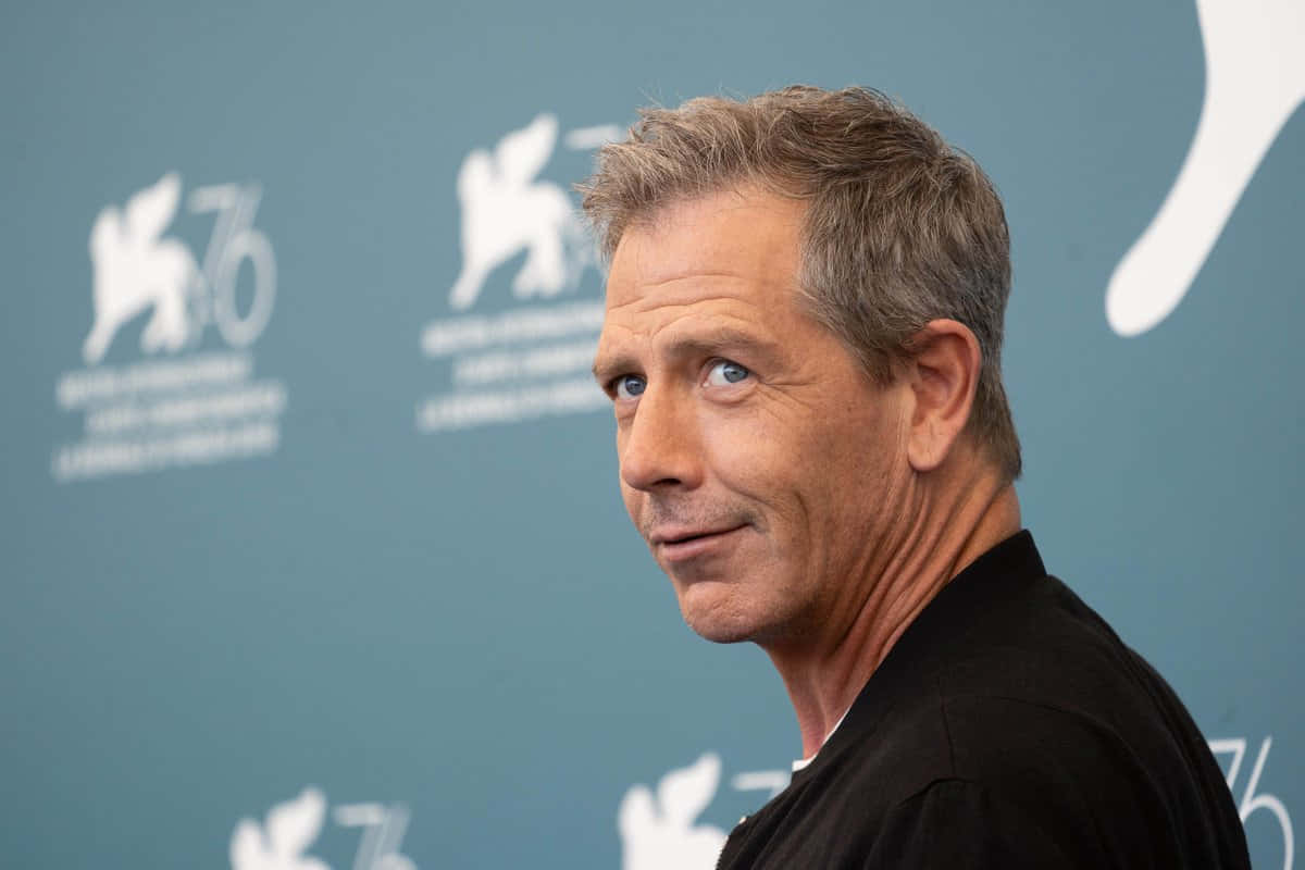 Ben Mendelsohn, blue backdrop, white logos, SD Desktop Wallpaper