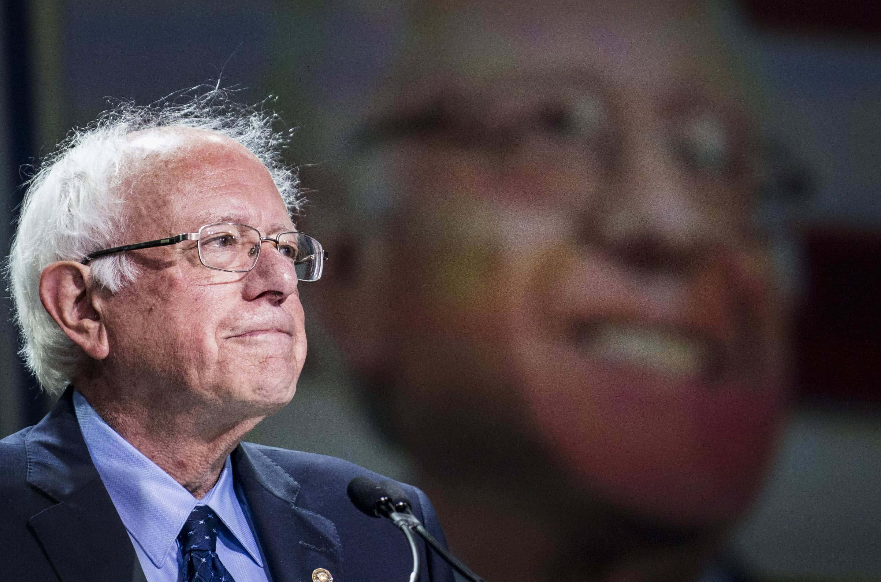 Bernie Sanders, podium, blurred large portrait of himself, 2K Desktop Wallpaper