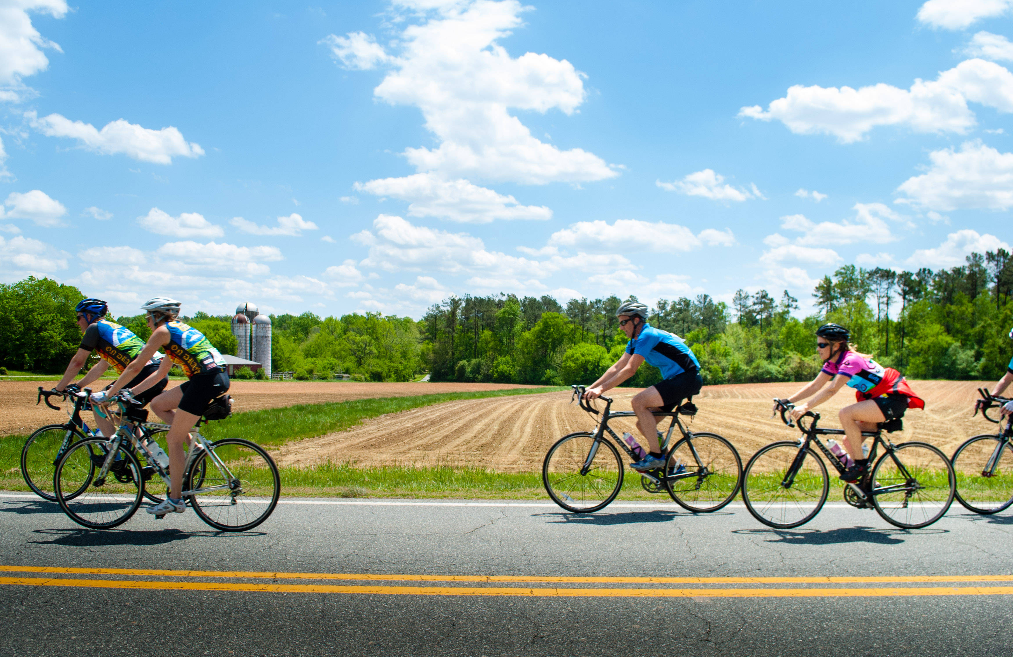 Bike Group Ride, sunlit rural road, bright blue sky, 2K Desktop Wallpaper