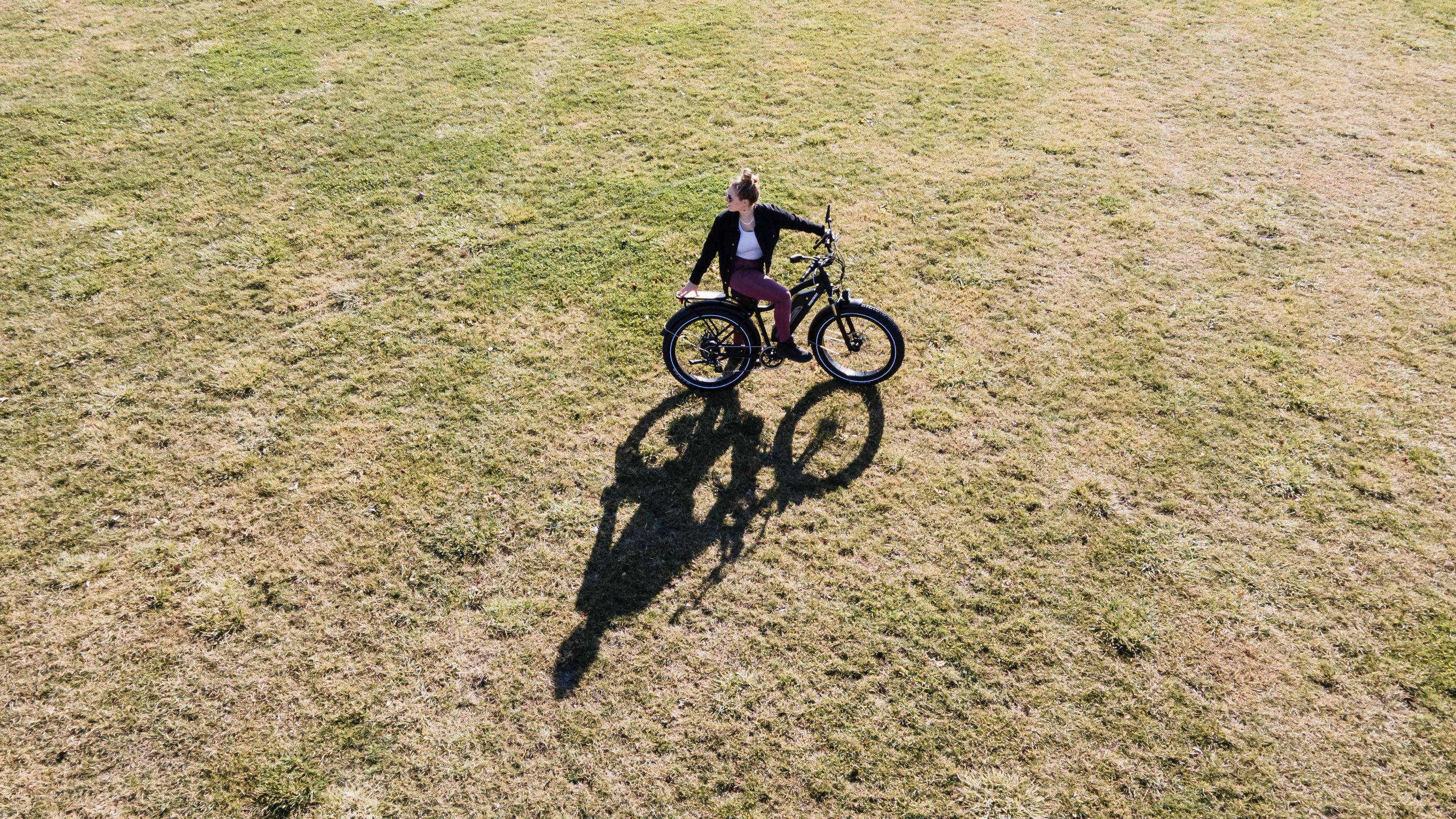 black electric bike, vast dry grass field, bright sunlight, 2K Desktop Wallpaper