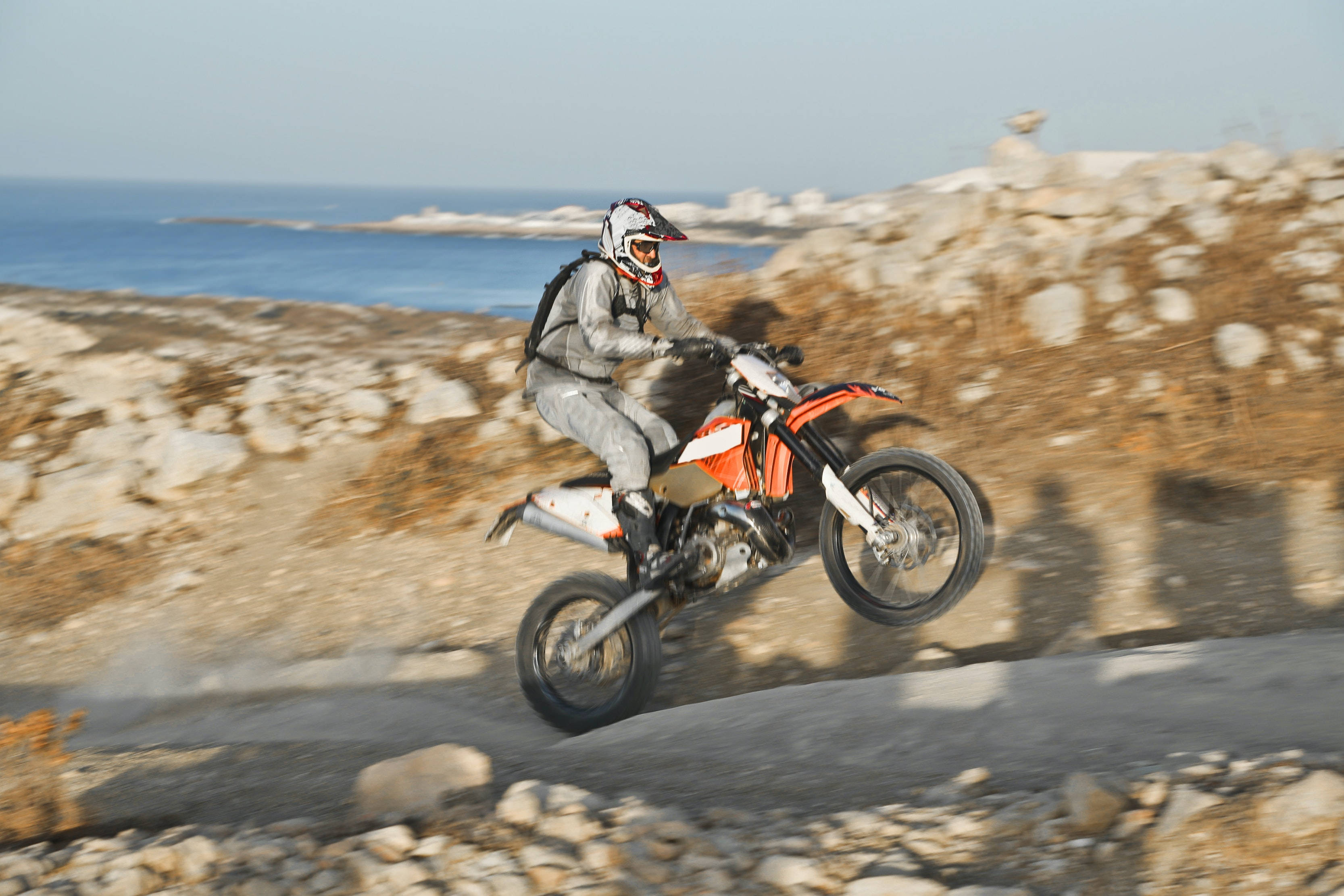 dirt bike, vibrant orange, rocky coastal path, 2K Desktop Wallpaper