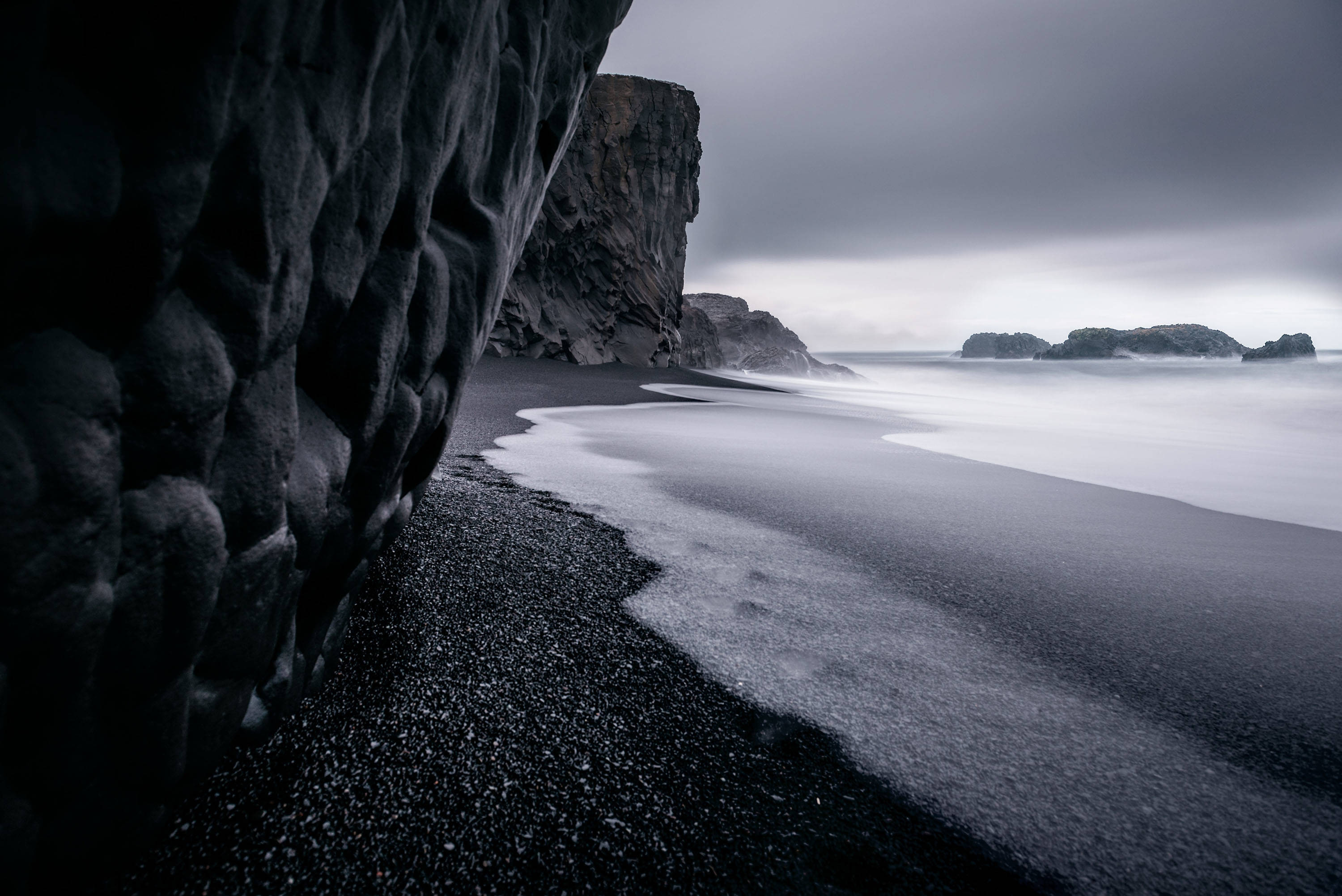 black sand beach, textured volcanic cliffs, gray overcast sky, 2K Desktop Wallpaper