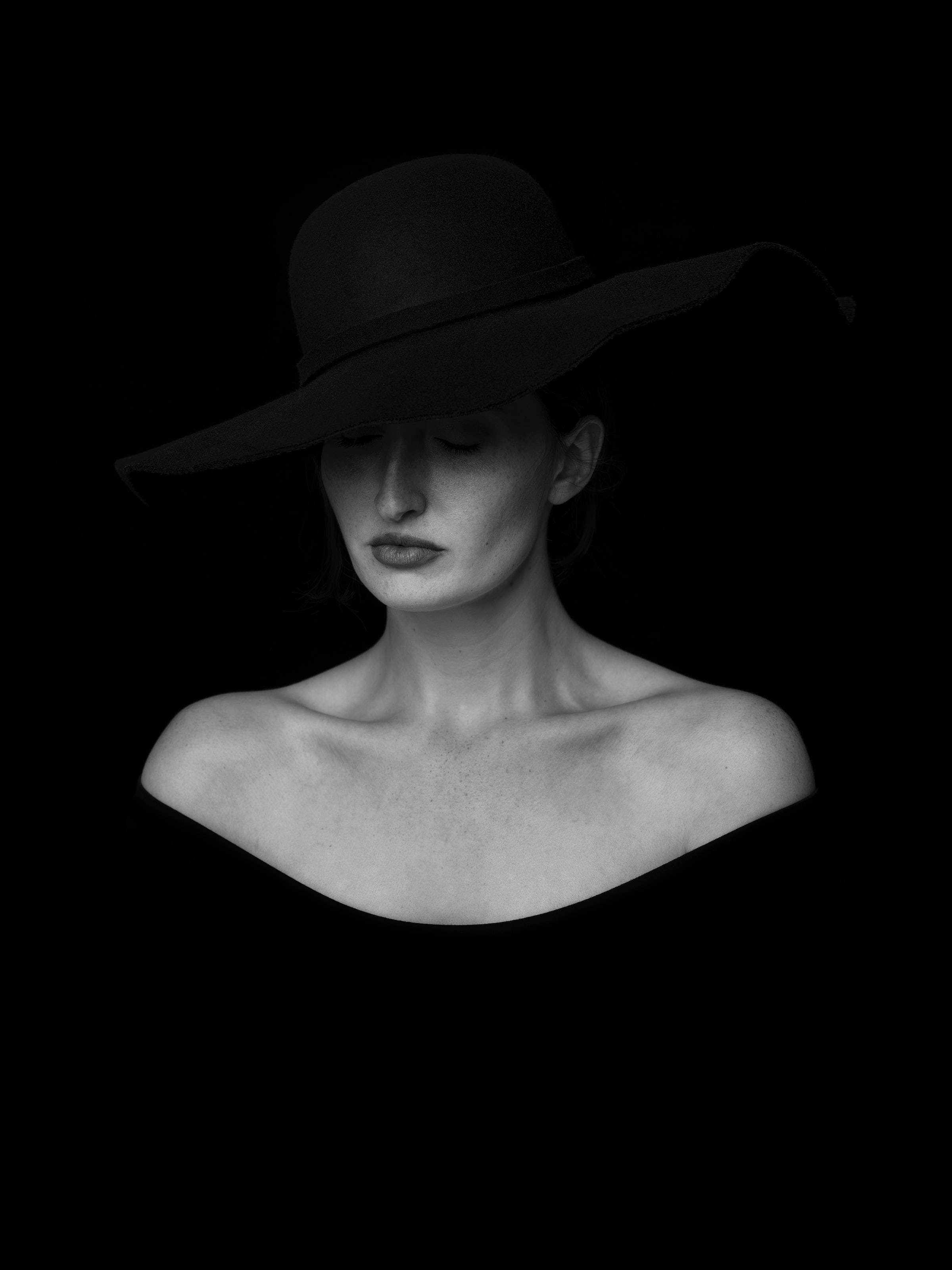 wide-brimmed black hat, pure black background, stark monochrome portrait, 2K Phone Wallpaper