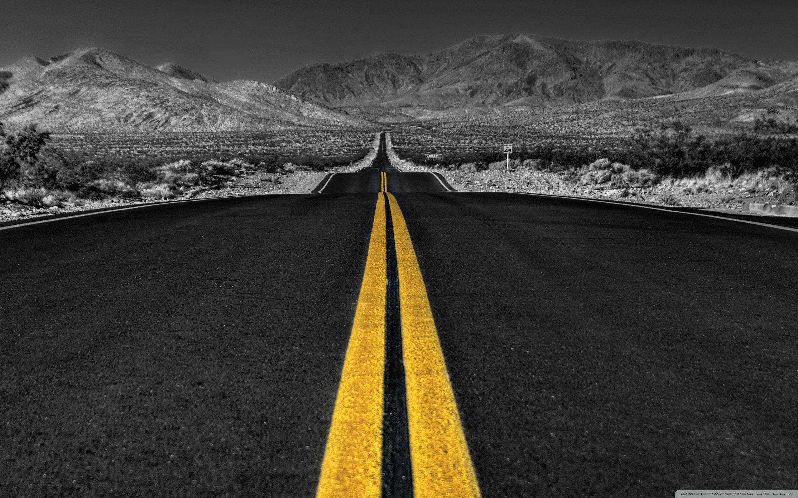 black and white desert highway, distant mountains, vibrant yellow center lines, 2K Desktop Wallpaper