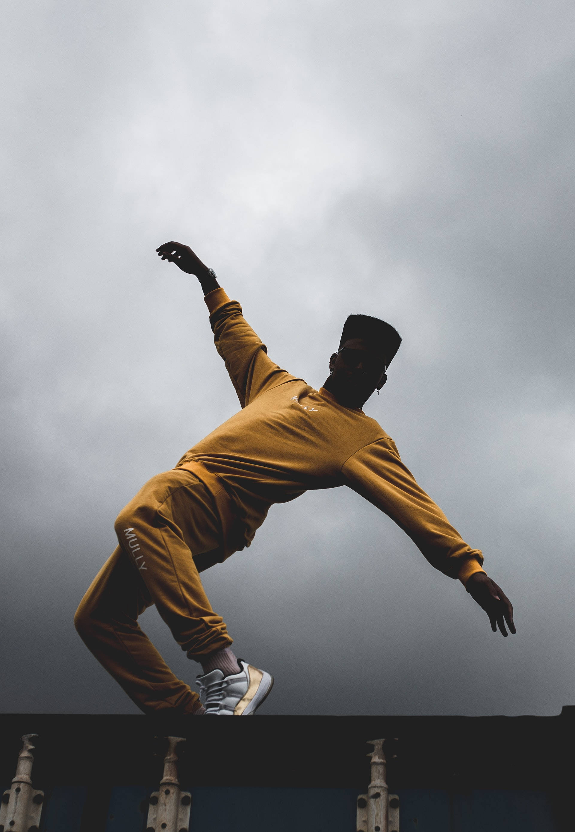 mustard yellow tracksuit, moody overcast sky, leaps dynamically, 2K Phone Wallpaper