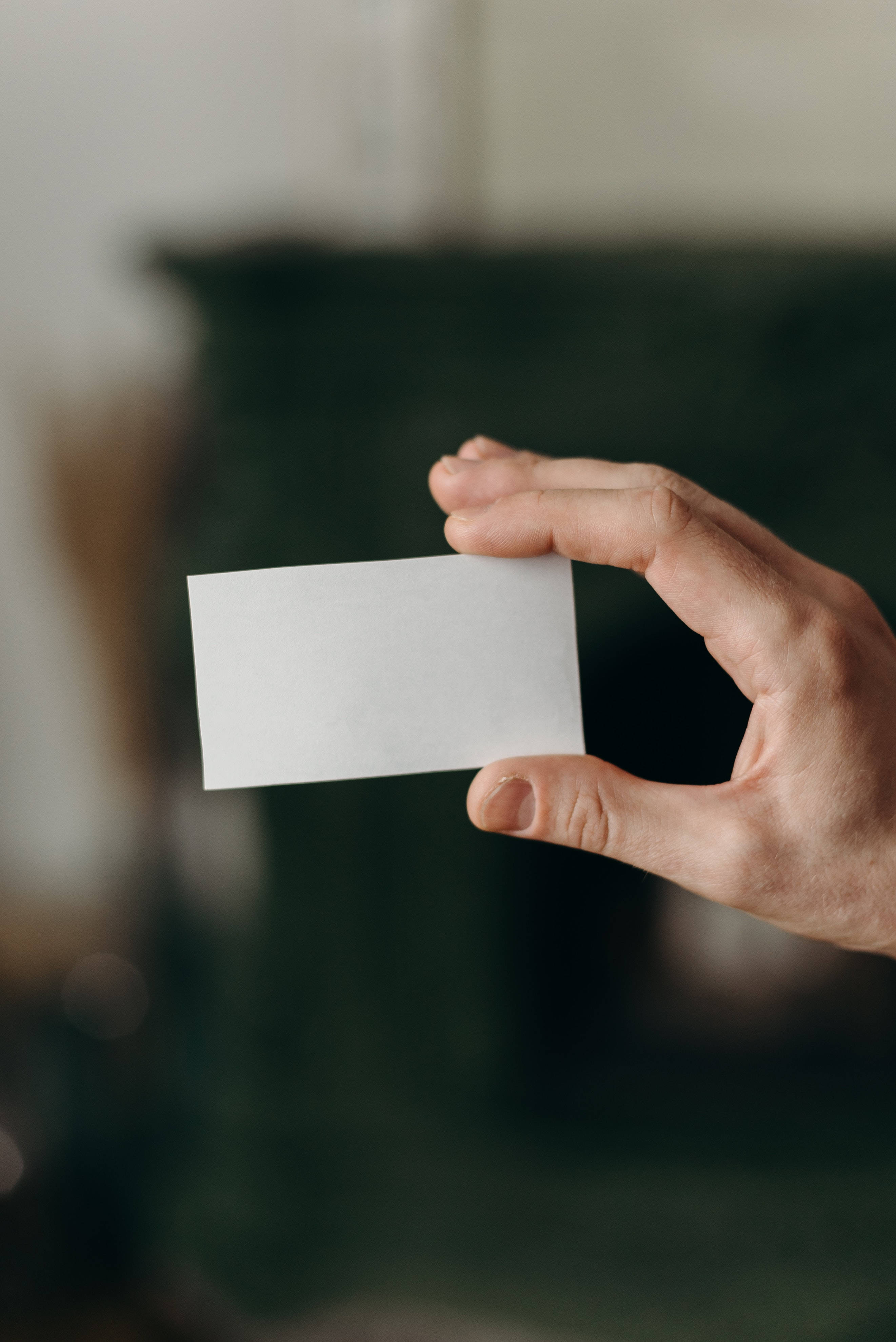 blank white business card, softly blurred dark green background, hand, 4K Phone Wallpaper