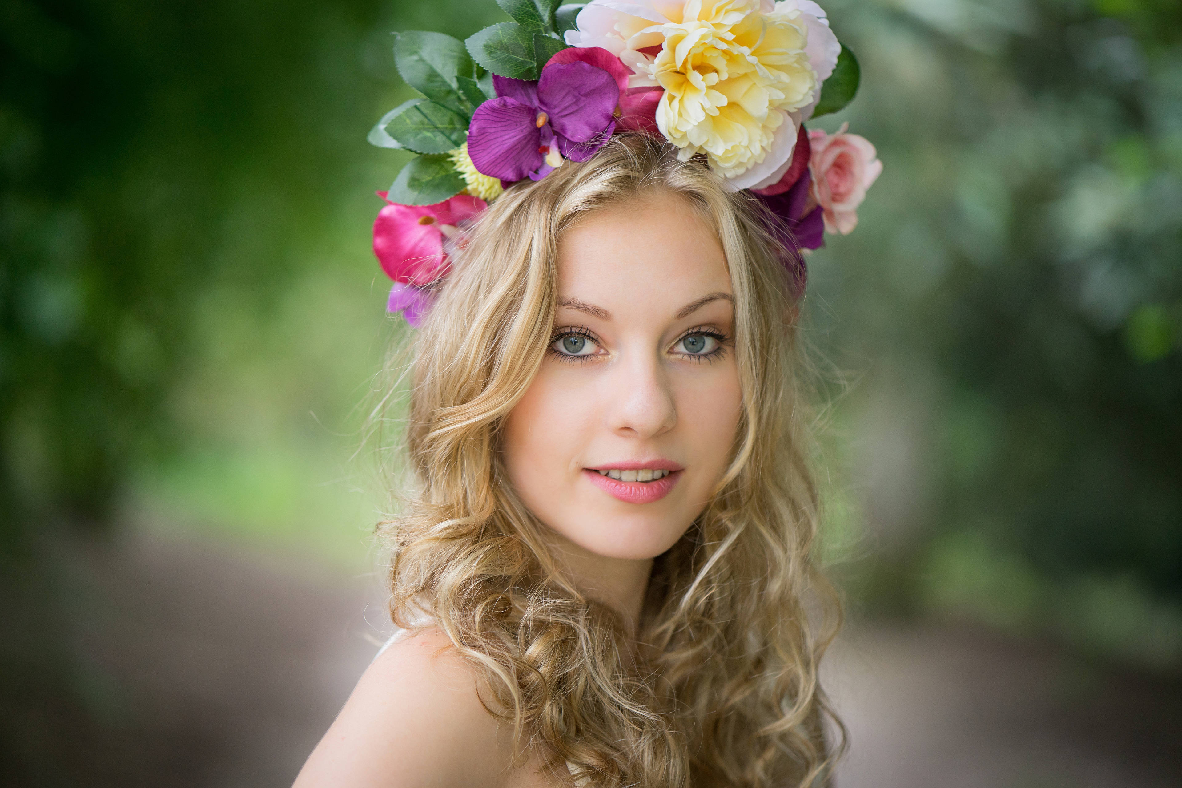 blonde female model, vibrant floral crown, soft green blurred garden backdrop, 4K Desktop Wallpaper