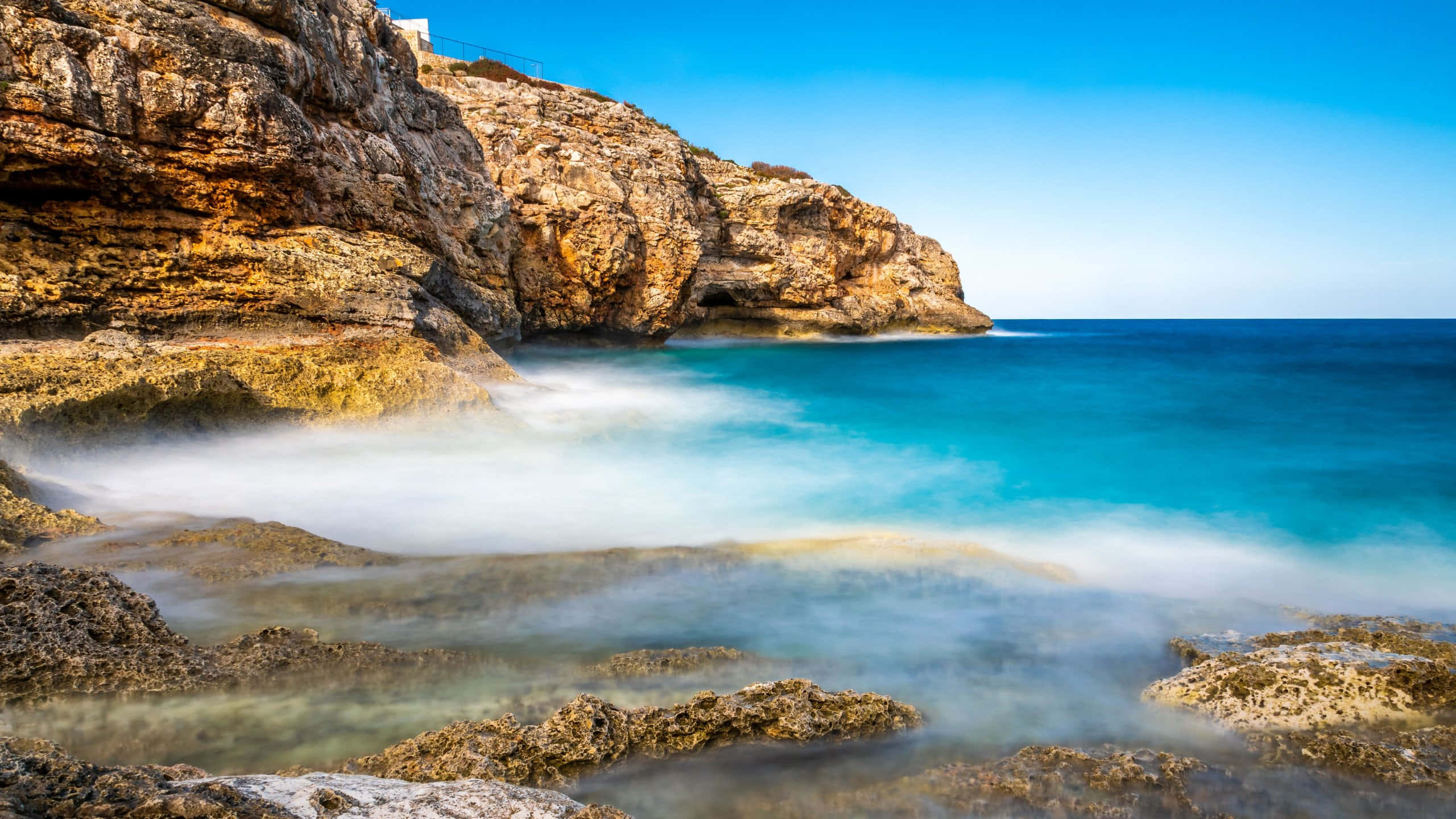 turquoise waves, rugged golden-brown cliffs, clear blue sky, 2K Desktop Wallpaper