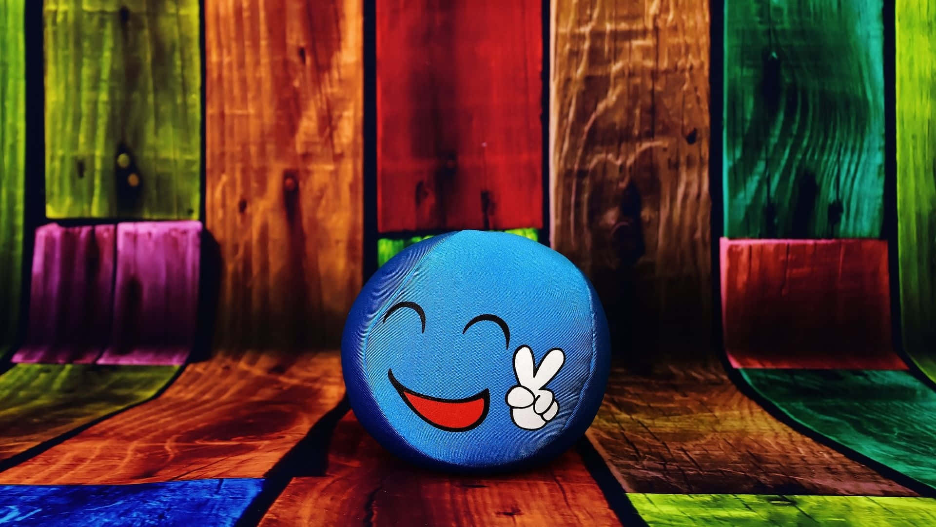 blue smiling plush ball, peace sign hand gesture, colorful wooden floor, Full HD Desktop Wallpaper