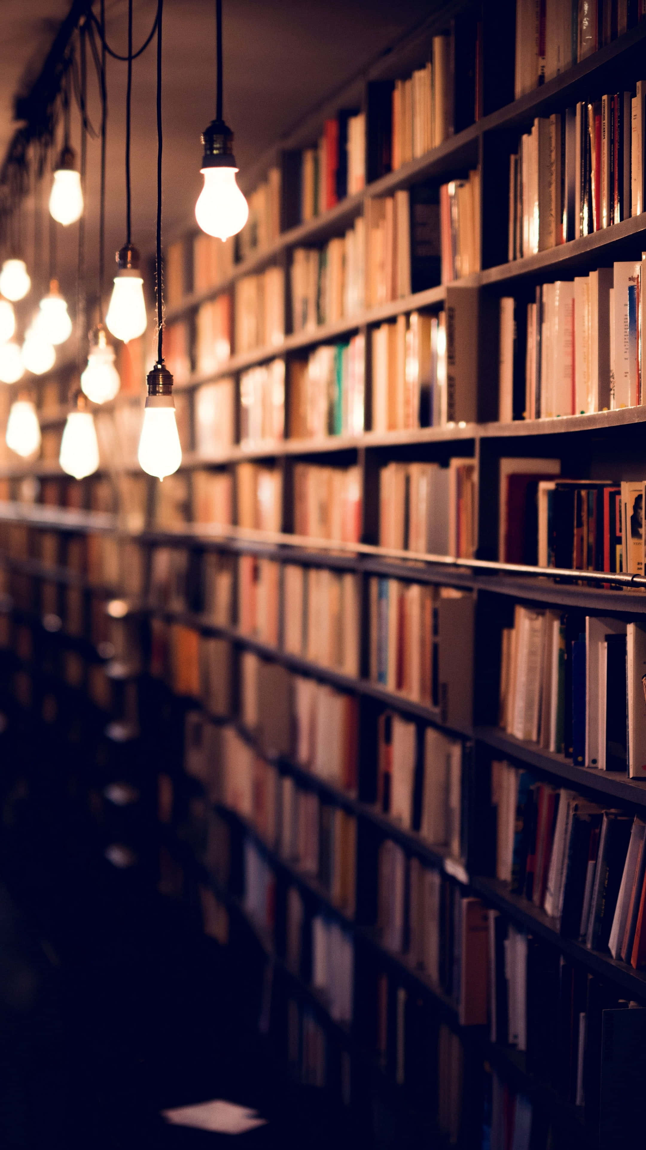 Books iPhone, library aisle, warm glowing bulbs, 4K Phone Wallpaper