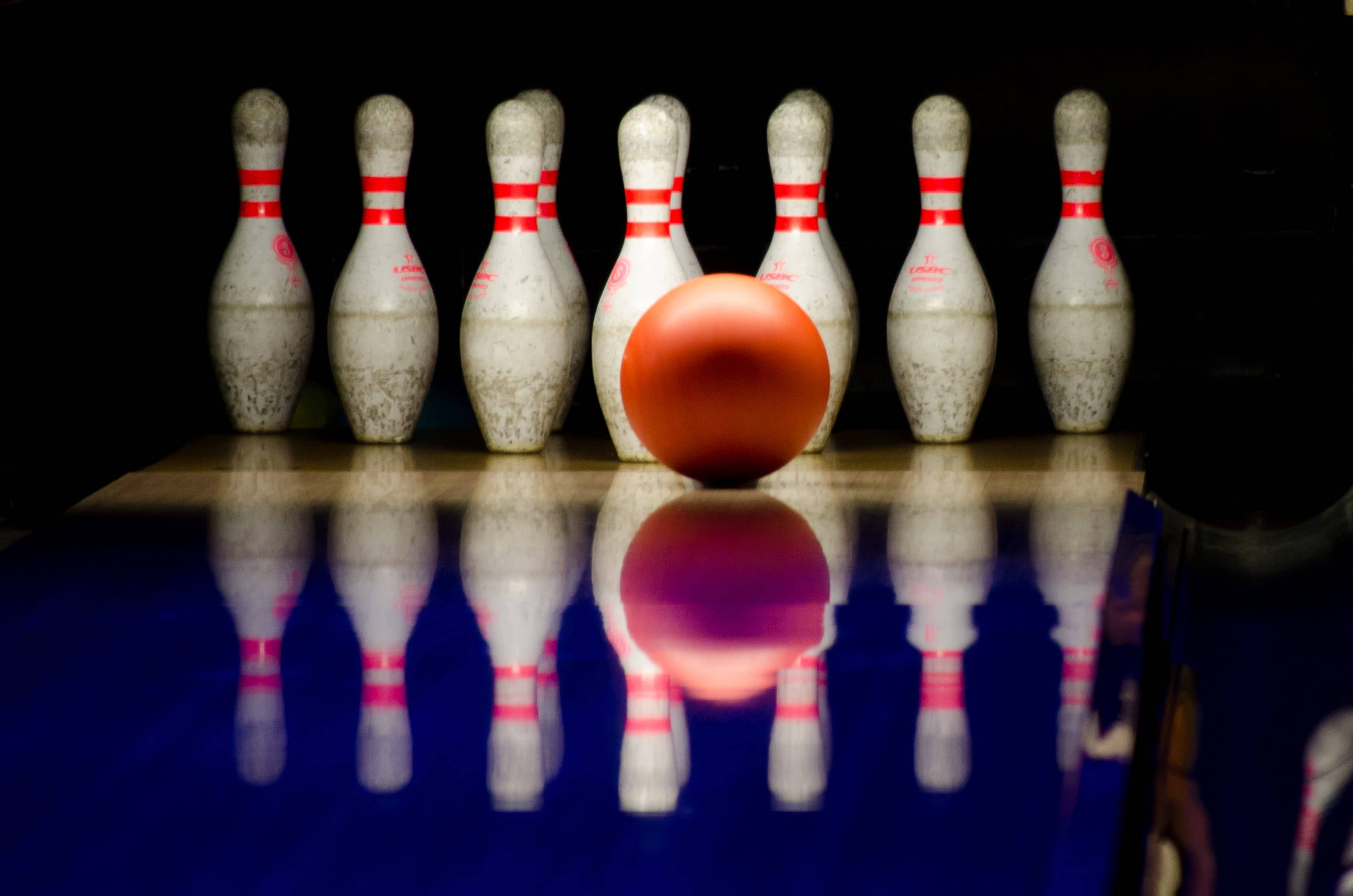 glossy orange bowling ball, worn white pins with red stripes, reflective blue lane, 2K Desktop Wallpaper